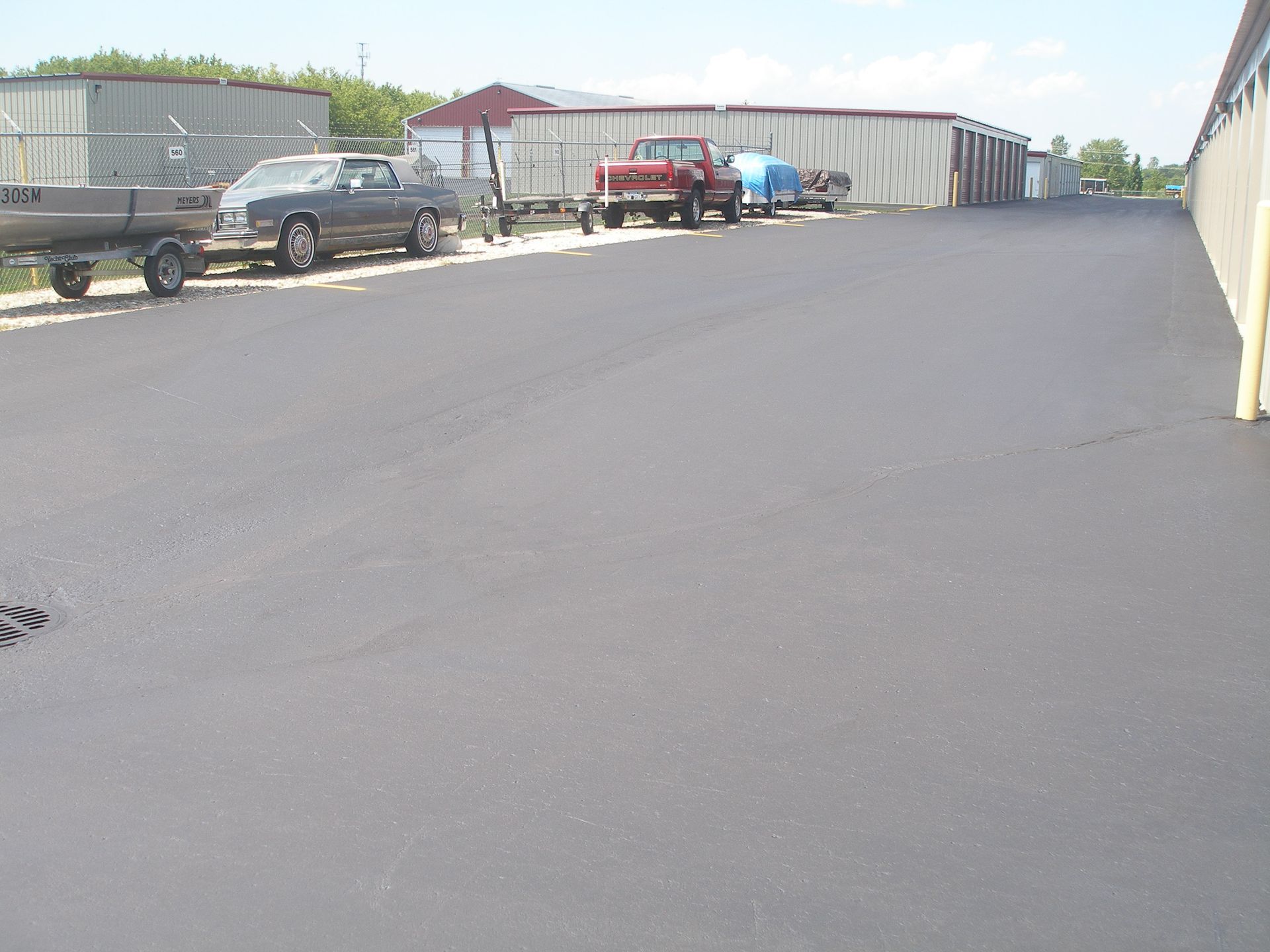 Asphalt parking area with vehicles parked along a row of storage units.