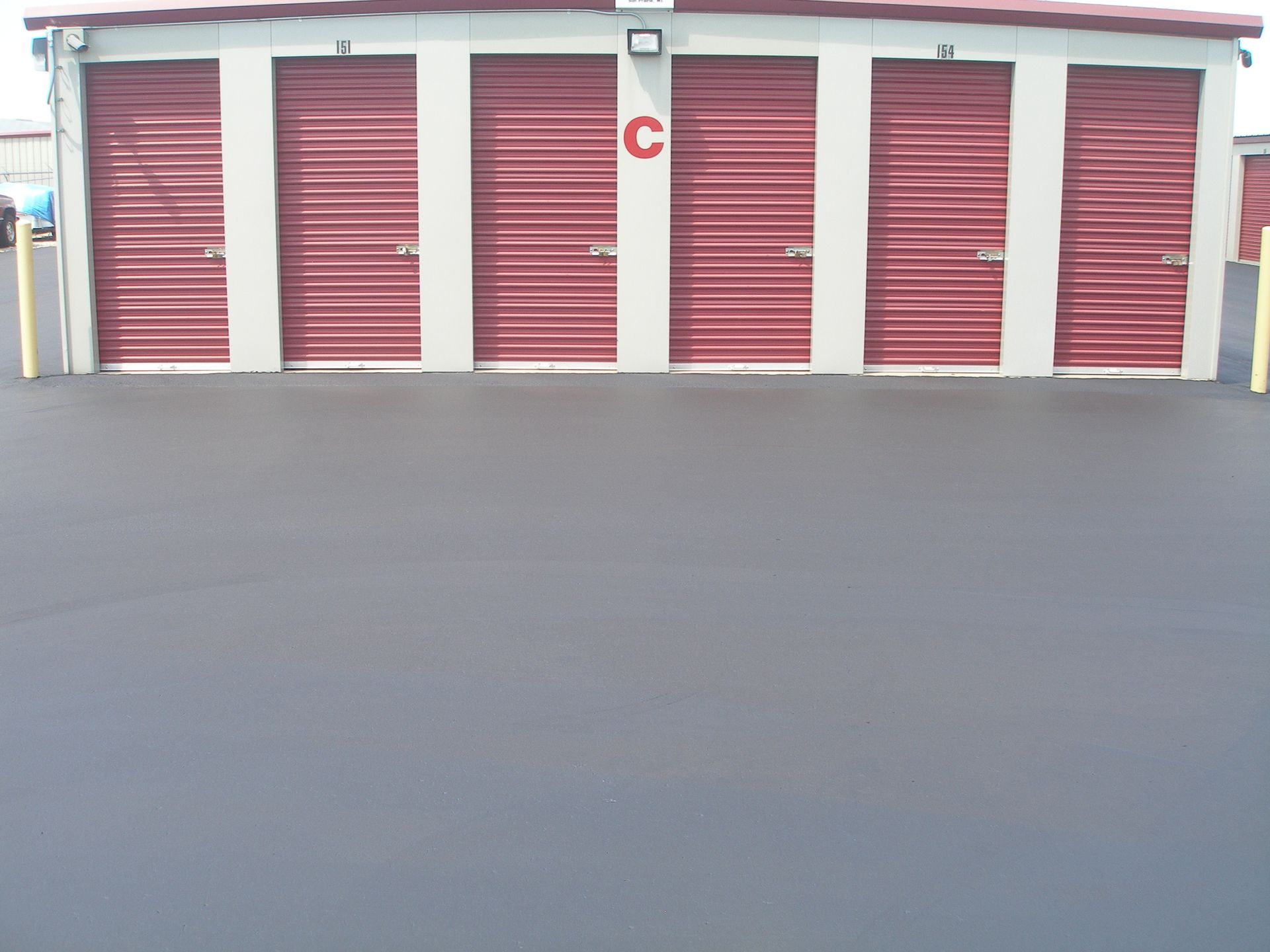Storage units with red doors and white trim, located on a dark asphalt surface, labeled 