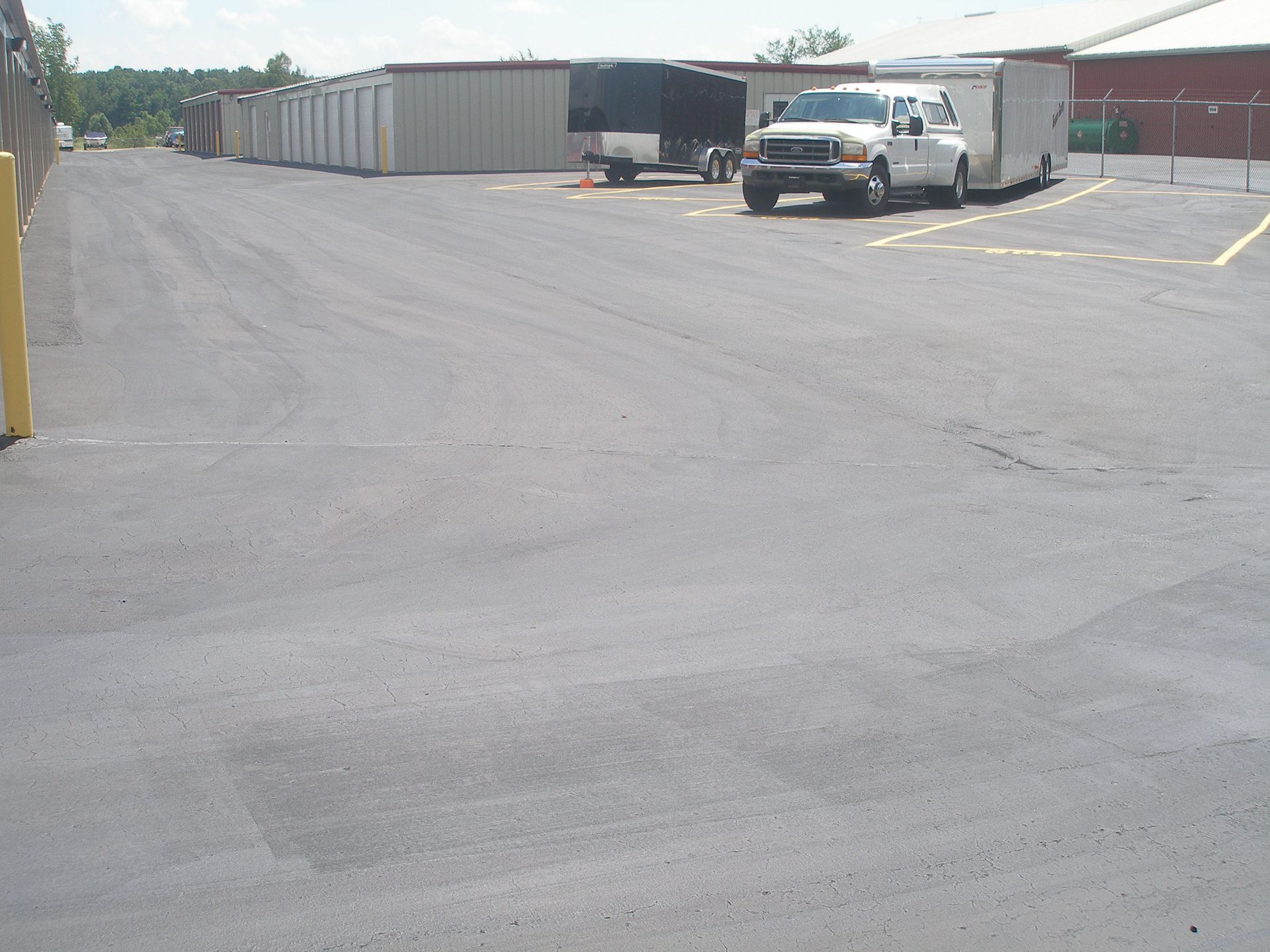 Asphalt parking lot with storage units and a truck with a trailer.