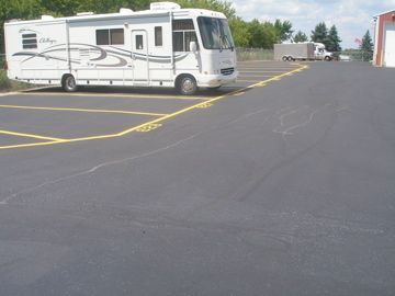 RV parked in an asphalt lot marked with yellow lines; a truck is in the distance.