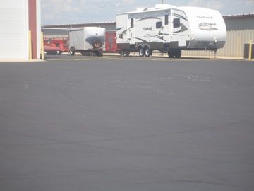 An RV and trailer parked on a paved lot in front of storage buildings.