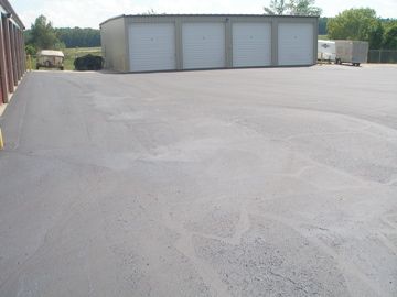 Exterior shot of a paved storage facility lot. Three garage doors in the background. Light grey asphalt.