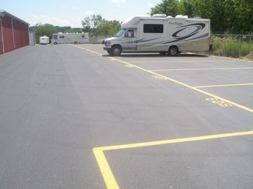 RV parked in a designated yellow-lined space at an outdoor storage facility; asphalt parking area.