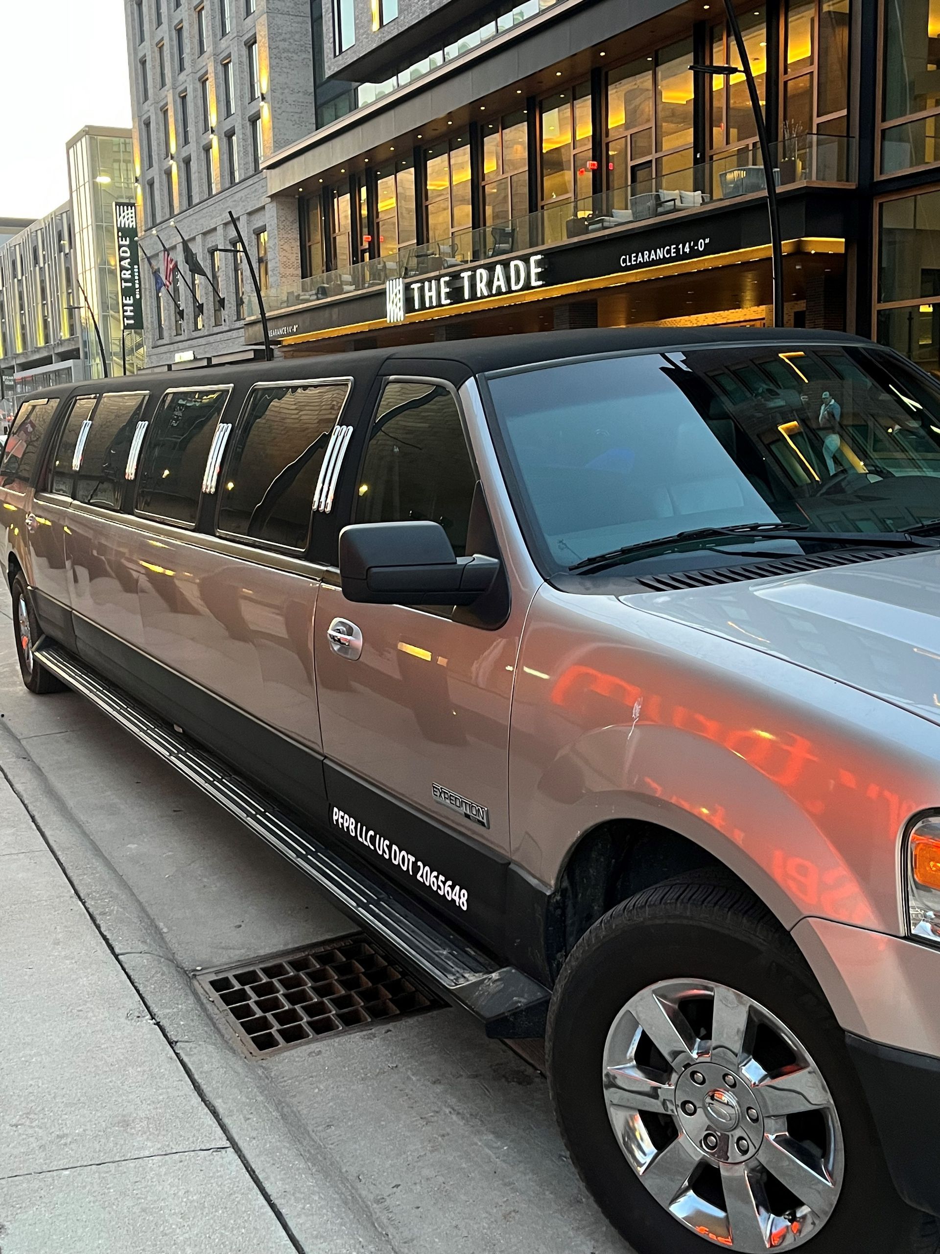 A silver limousine is parked on the side of the road in front of a building.