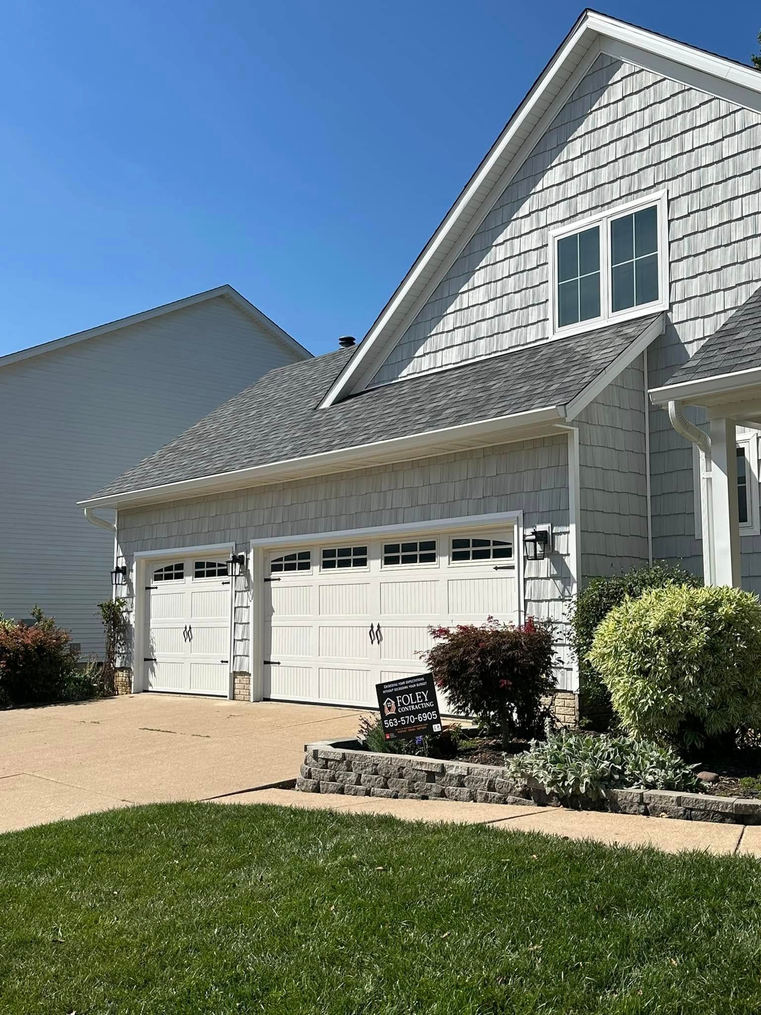 A white house with two garage doors and a gray roof.