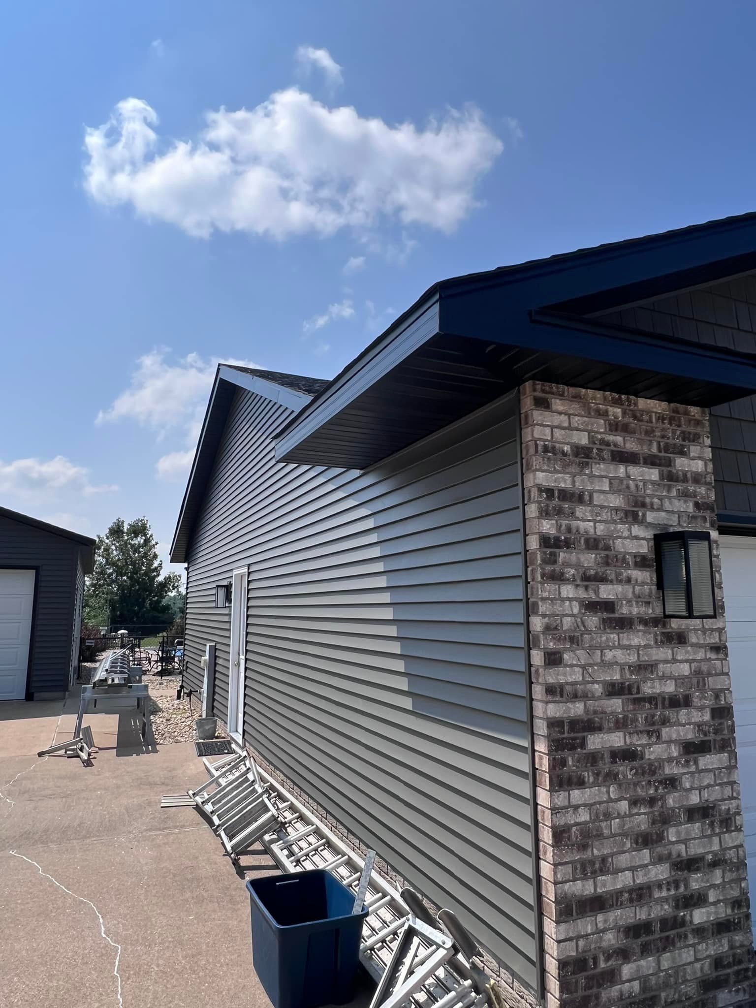 A house with a brick wall and siding is being painted on a sunny day.