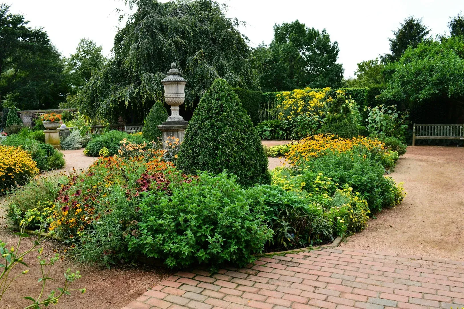 Landscaped garden with colorful flower beds, trimmed shrubs, a stone lamp, and a brick path