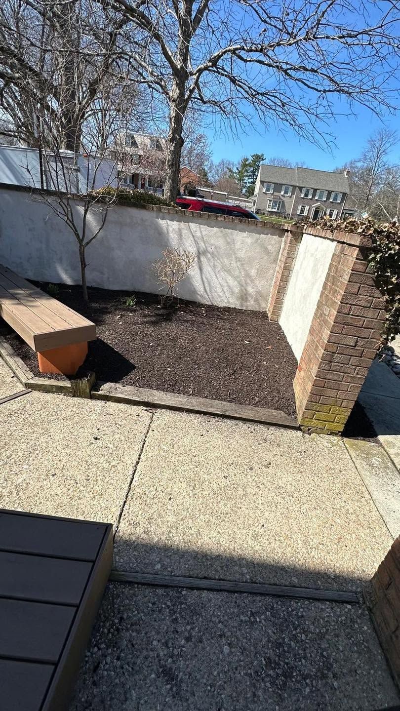 Backyard patio with white retaining wall, gravel bed, bare trees, and a red bench under blue sky