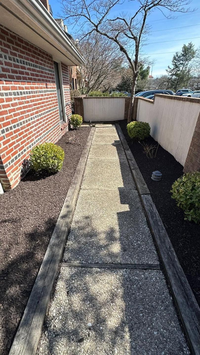 Narrow brick and concrete side yard with gravel borders, shrubs, and a fence at the end