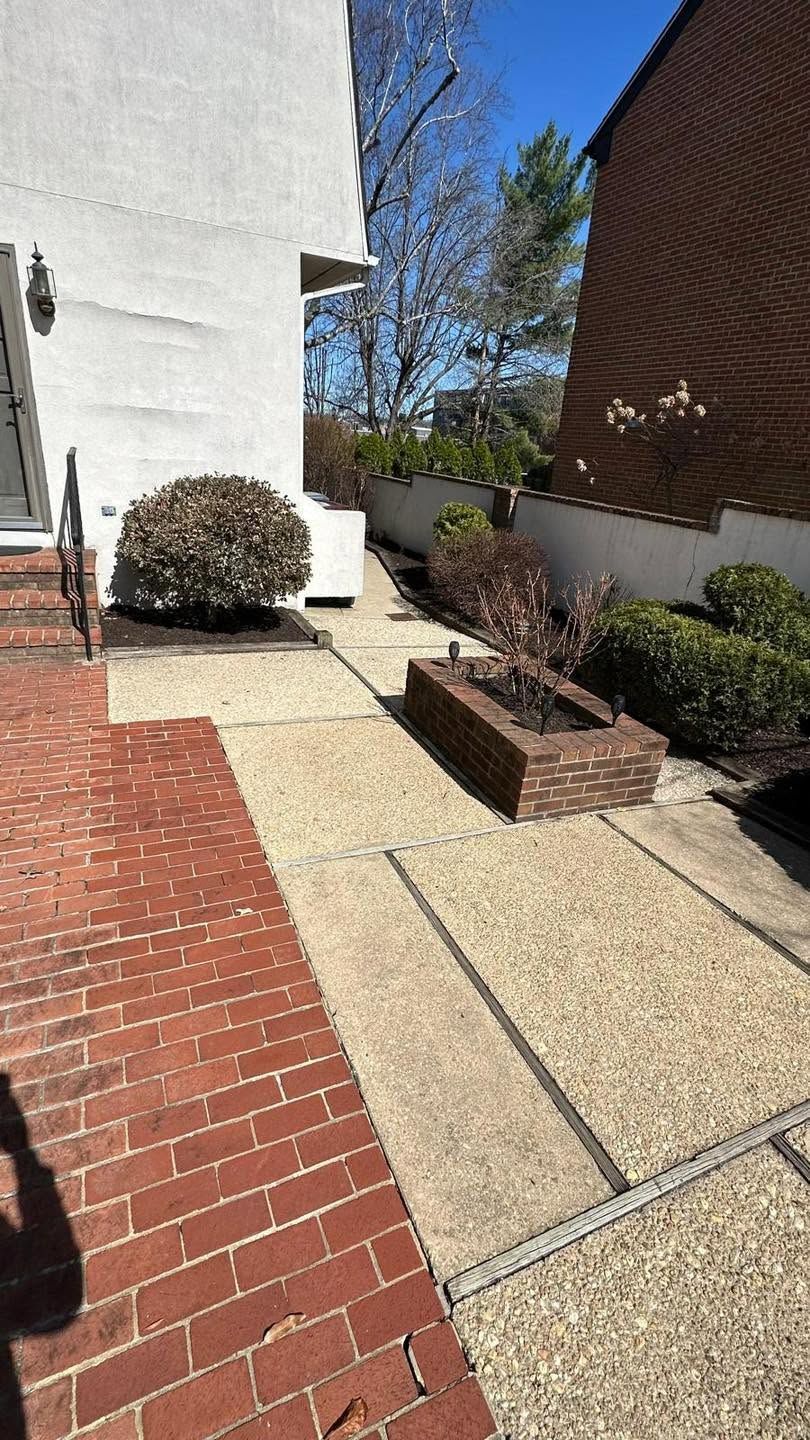 Brick walkway beside white building and landscaped bushes under a blue sky