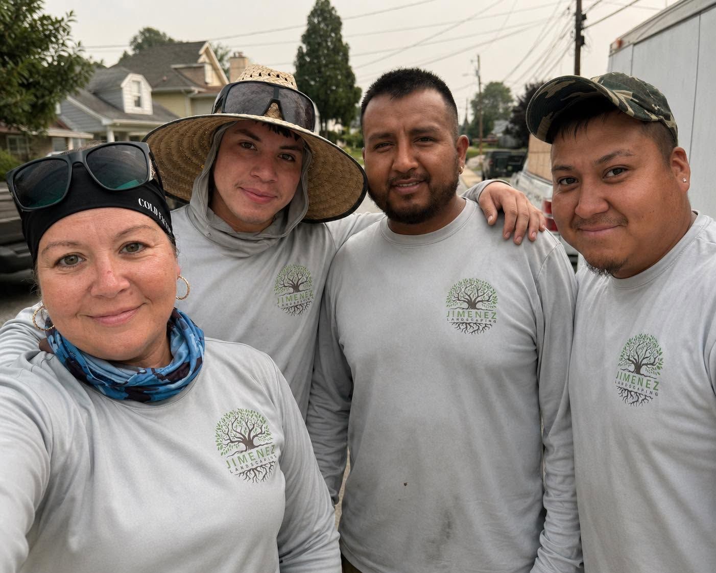 Four volunteers in matching white shirts posing outdoors on a street, smiling at the camera.