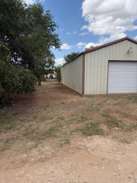 A white garage with a white garage door is sitting in the middle of a dirt field.