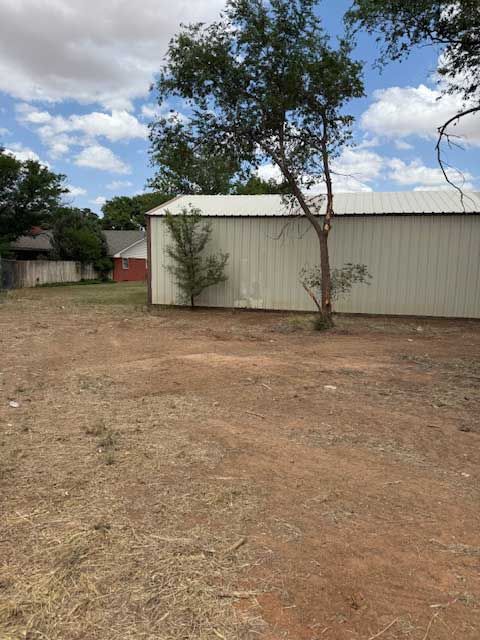 A white building with a tree in front of it in a dirt field.