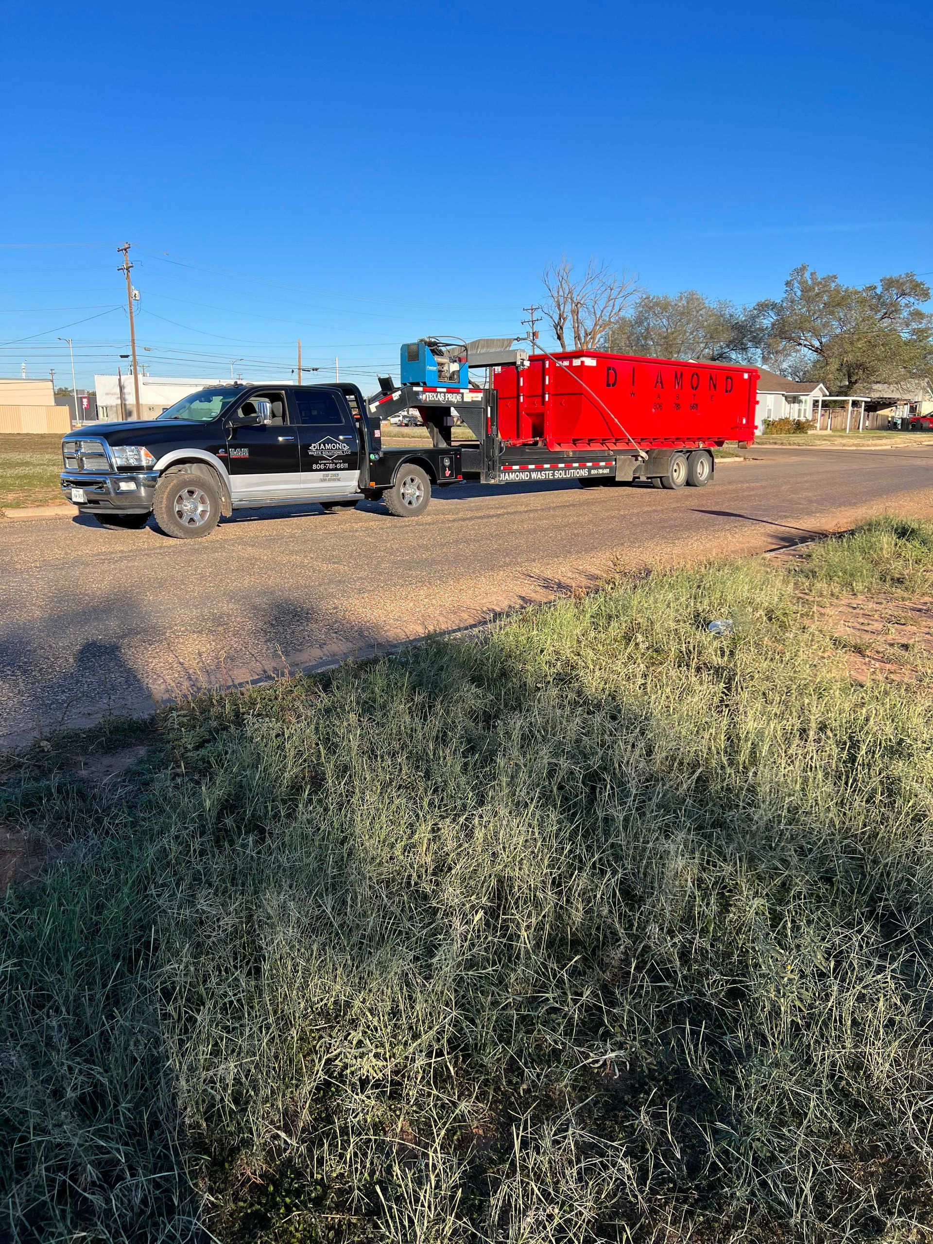 A black truck is towing a red dumpster on a trailer.