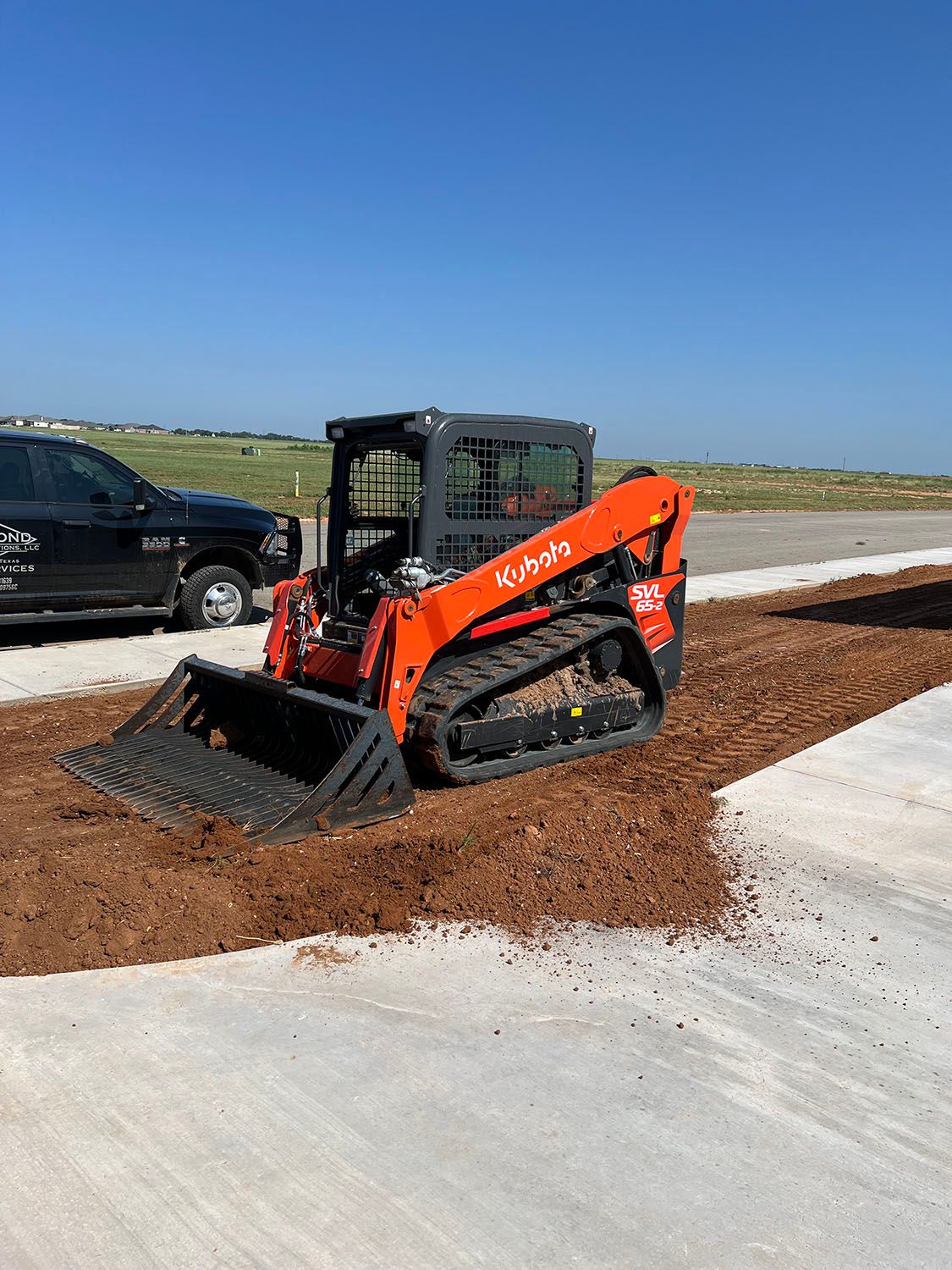 A skid steer compacting and smoothing dirt.