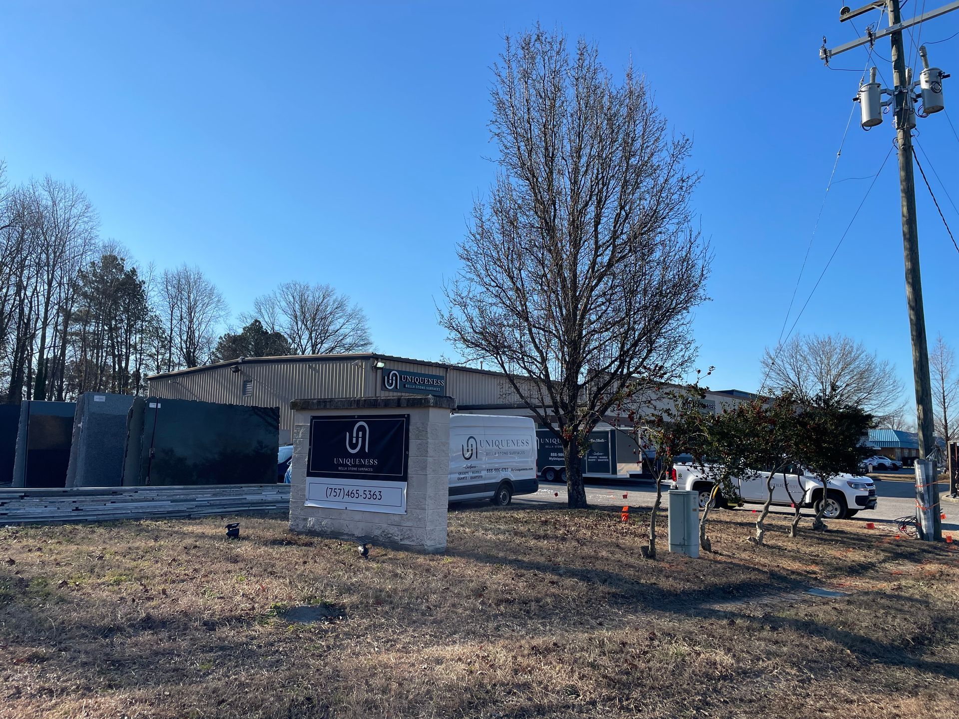 Sign in front of a building; daytime, blue sky, bare tree, utility pole, and a vehicle are present.