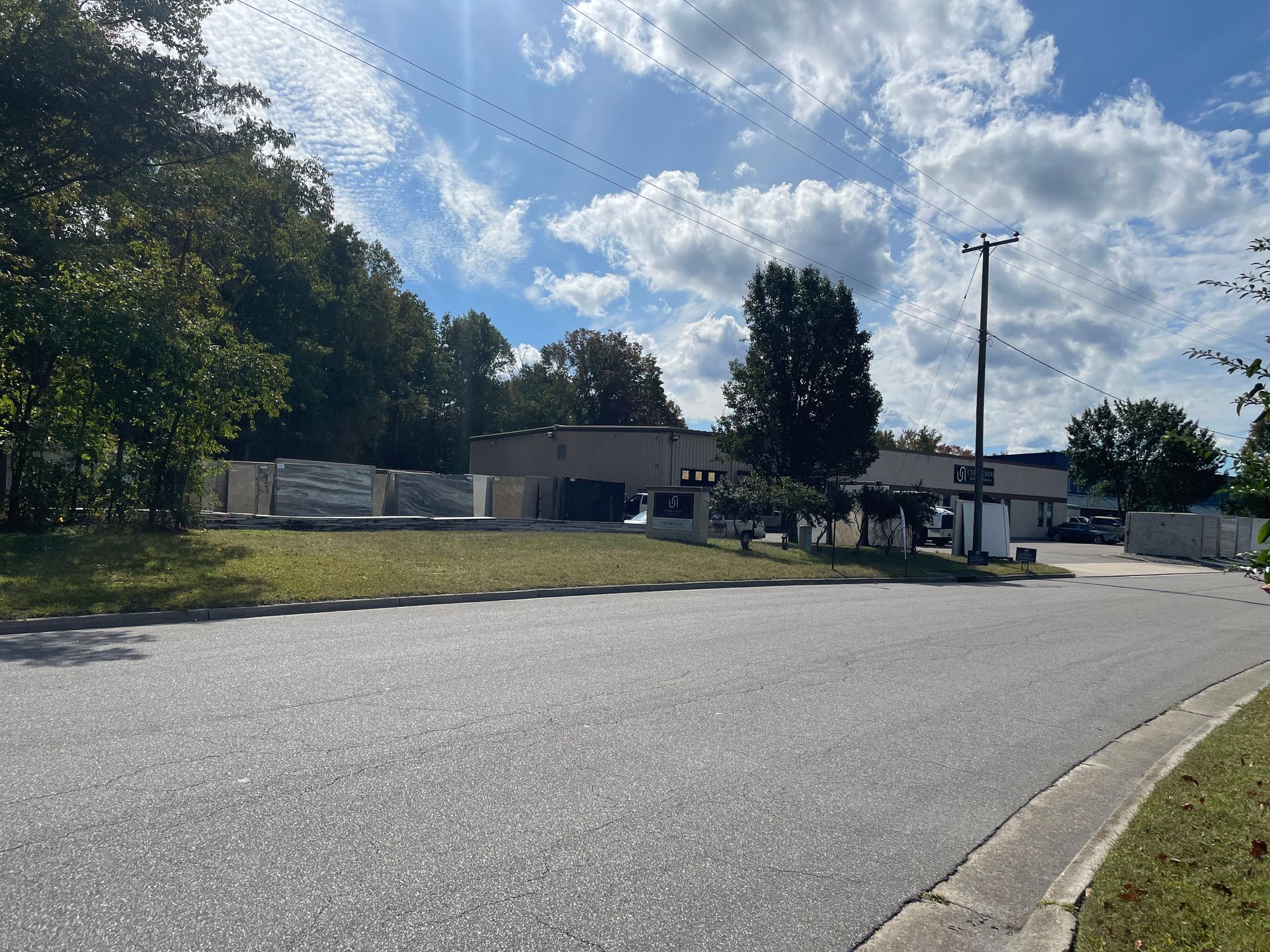 Paved road leads to a low-rise building under a cloudy sky, with trees on either side.