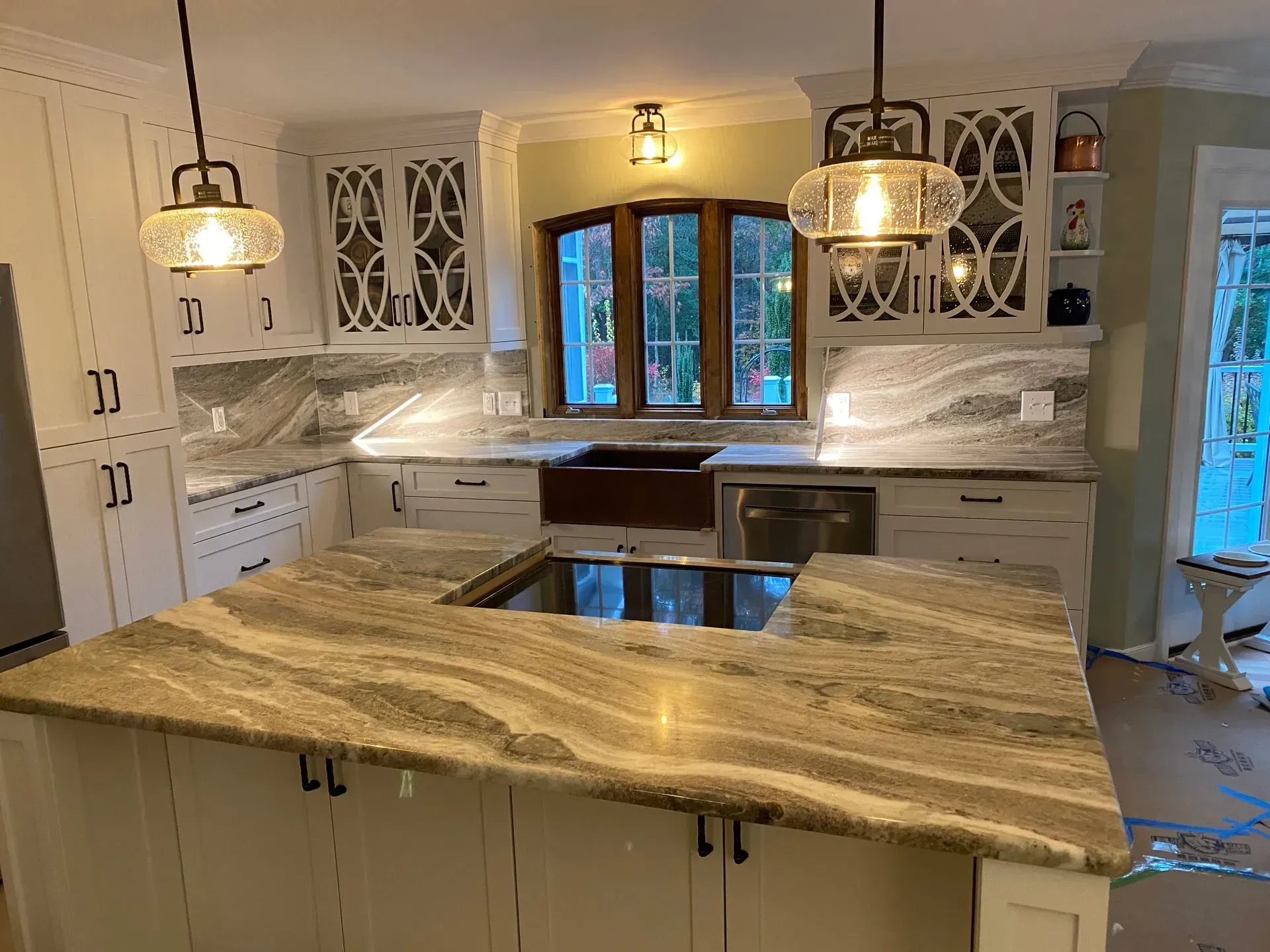 White kitchen with granite countertops, island with cooktop, and decorative pendant lights.