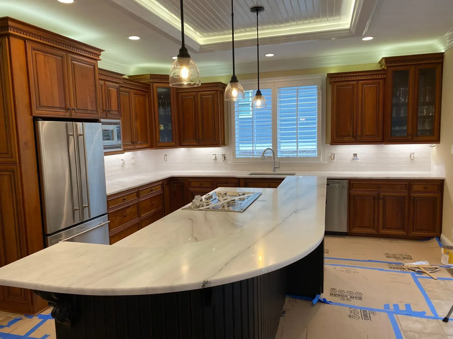 Kitchen with wooden cabinets, white countertop island, pendant lights, and stainless steel appliances.
