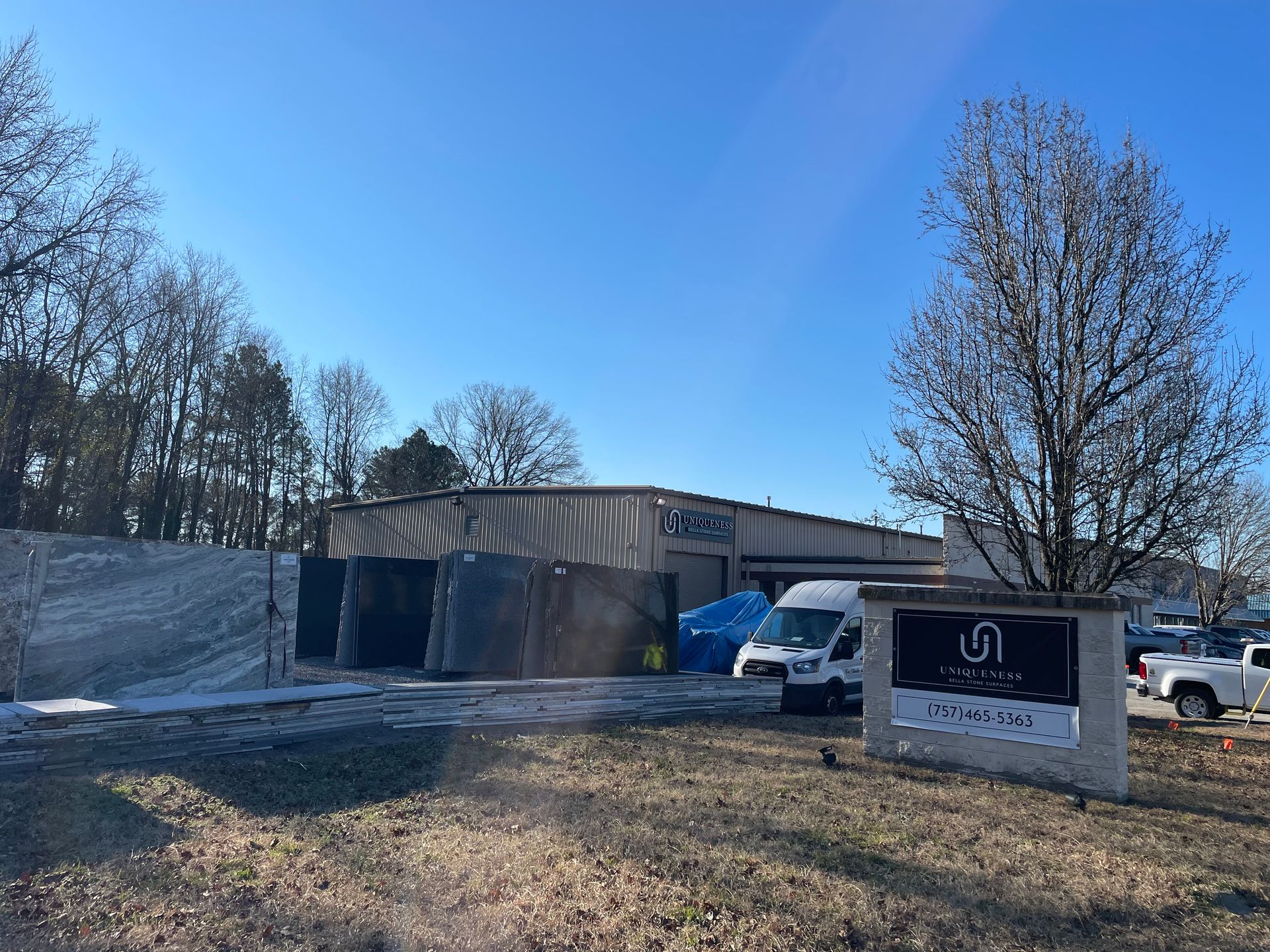 Exterior of building with sign, white van, and trees against a blue sky.