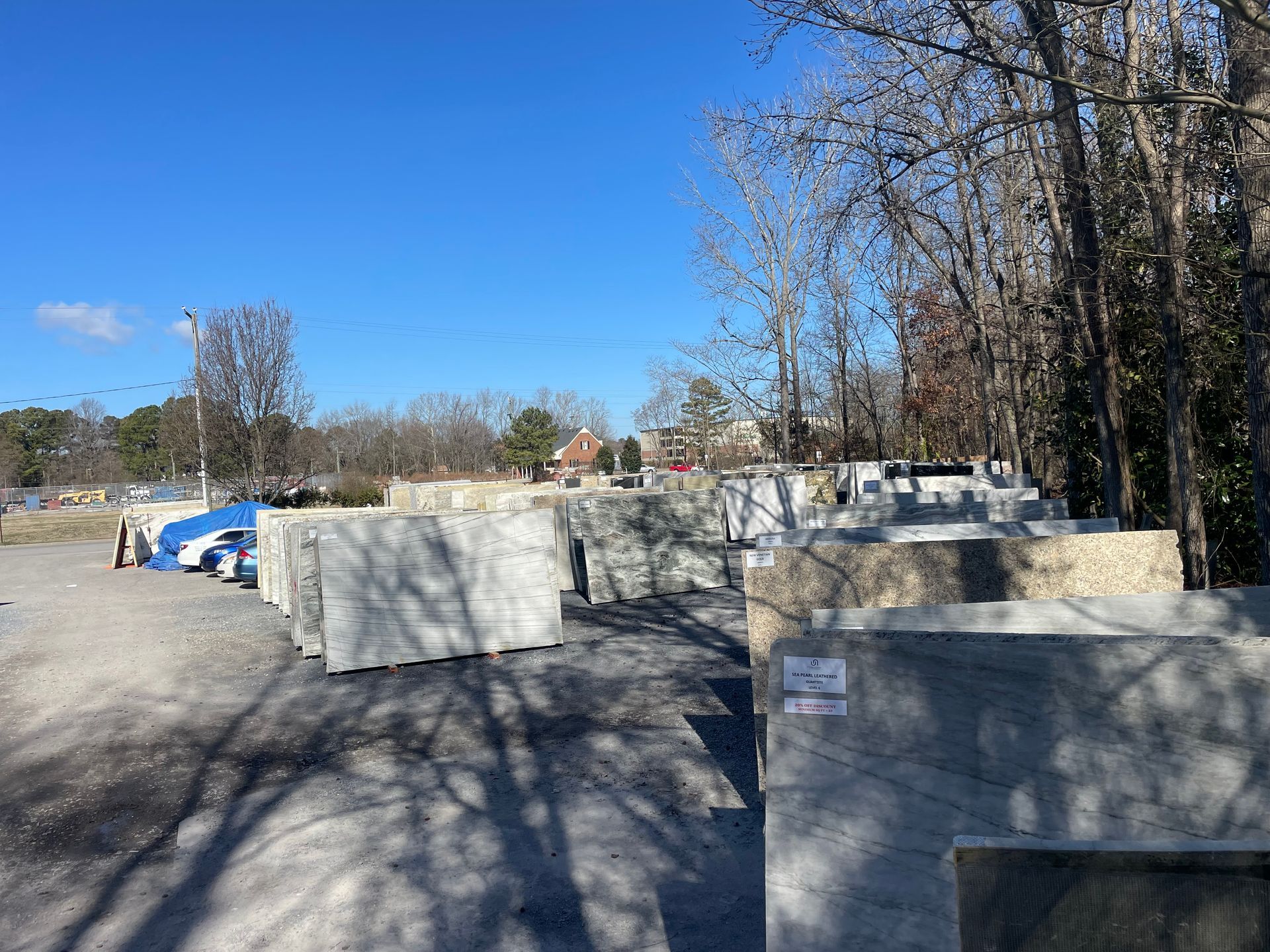 Outdoor stone slabs stacked in a yard, trees and clear sky in the background.