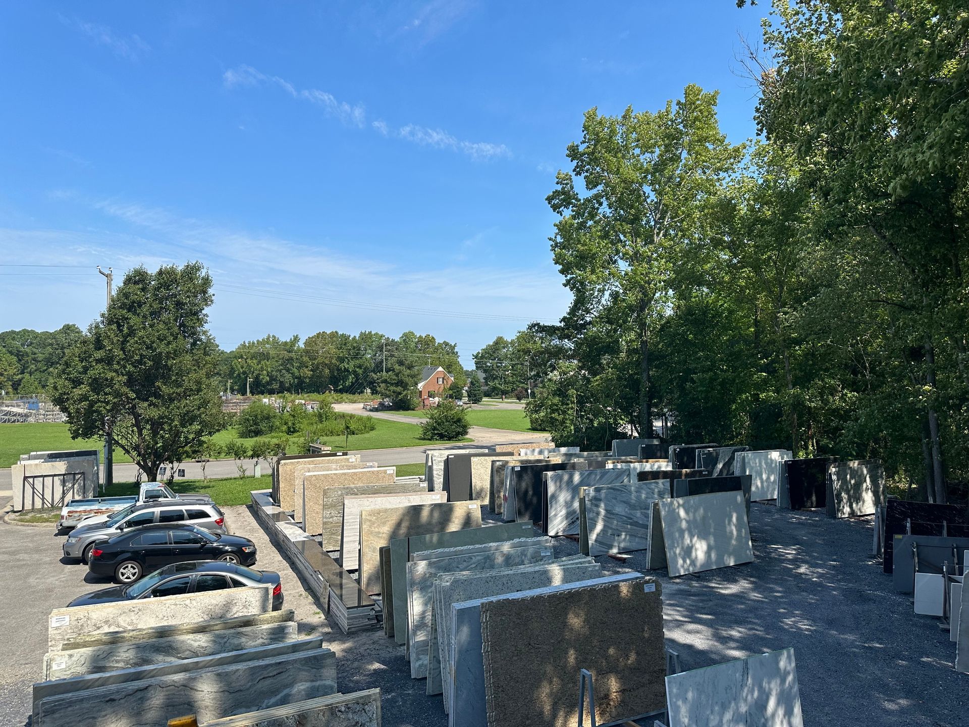 Large stone slabs displayed outside, with parked cars and trees in the background under a blue sky.