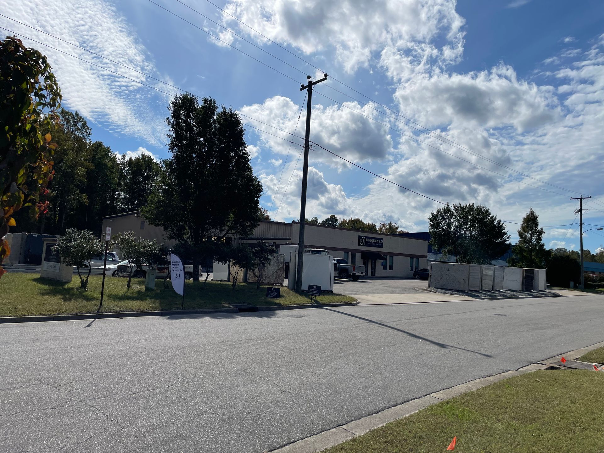 Exterior of a business building with parked cars, surrounded by trees and a cloudy sky.