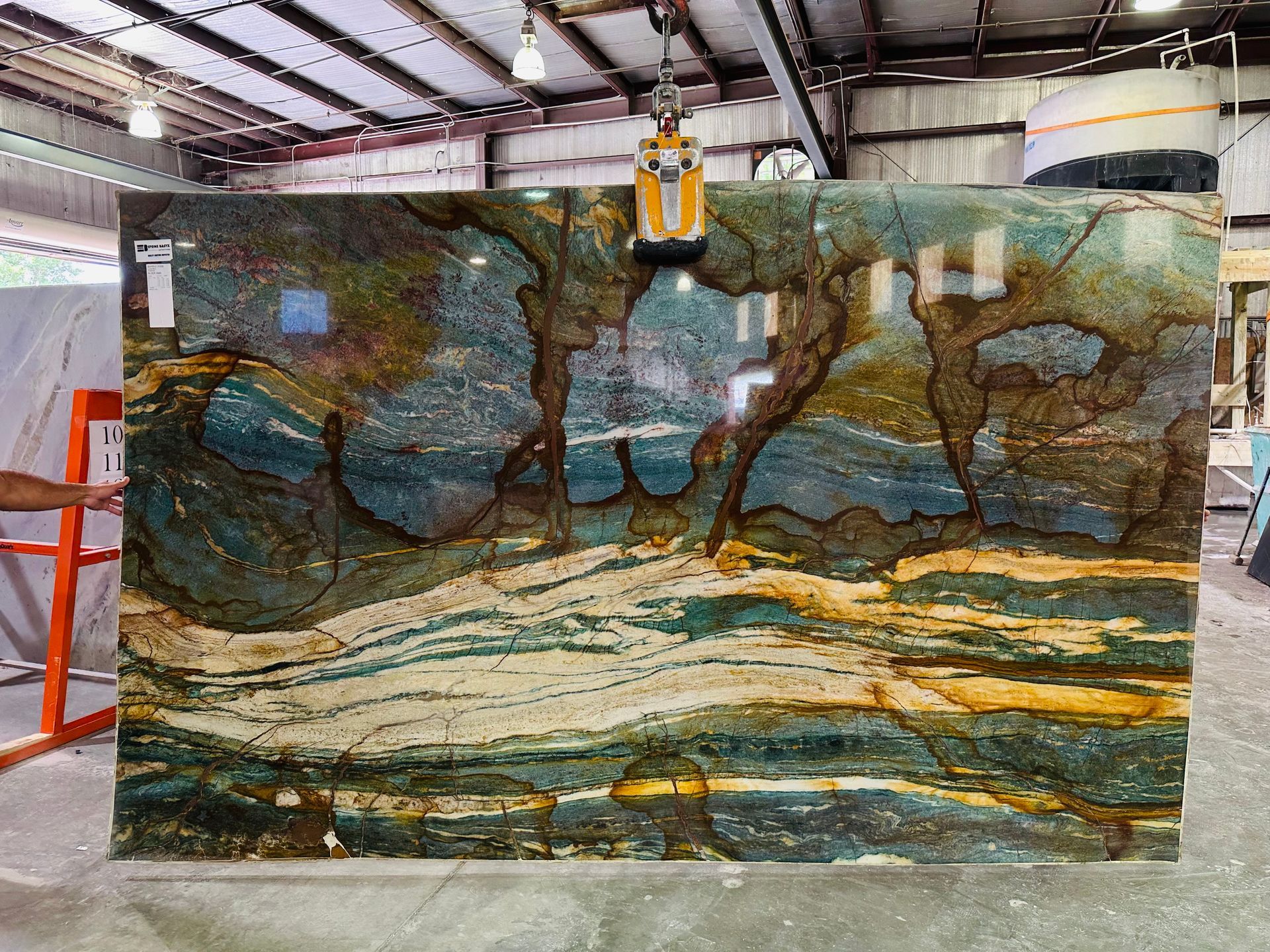 Large slab of stone with blue, brown, and gold veining in an industrial setting.