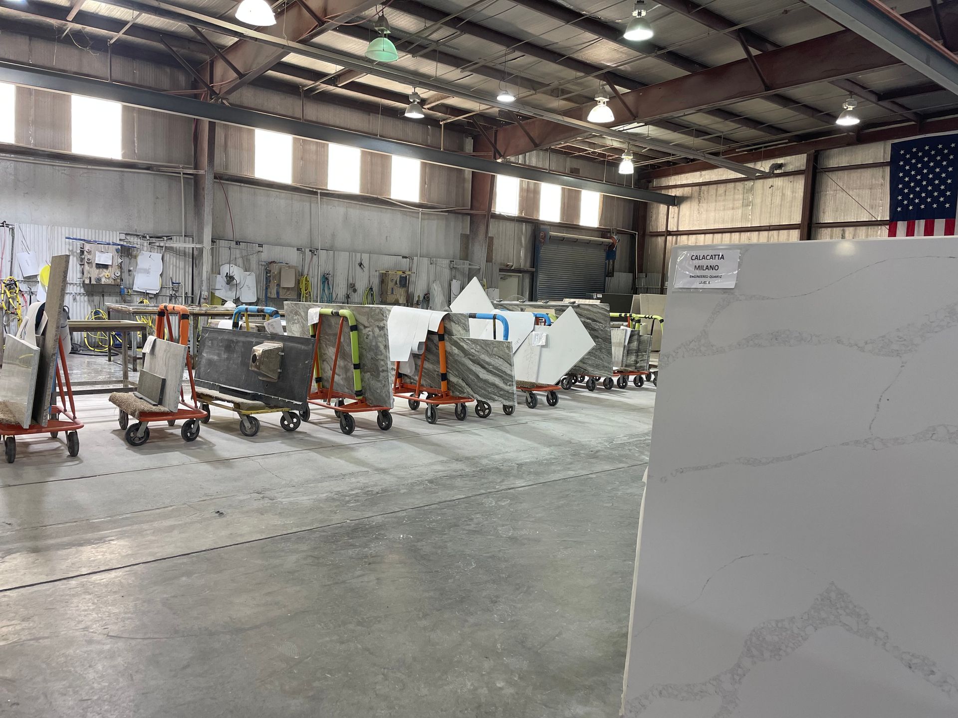 Warehouse interior with several stone slabs on carts, American flag.