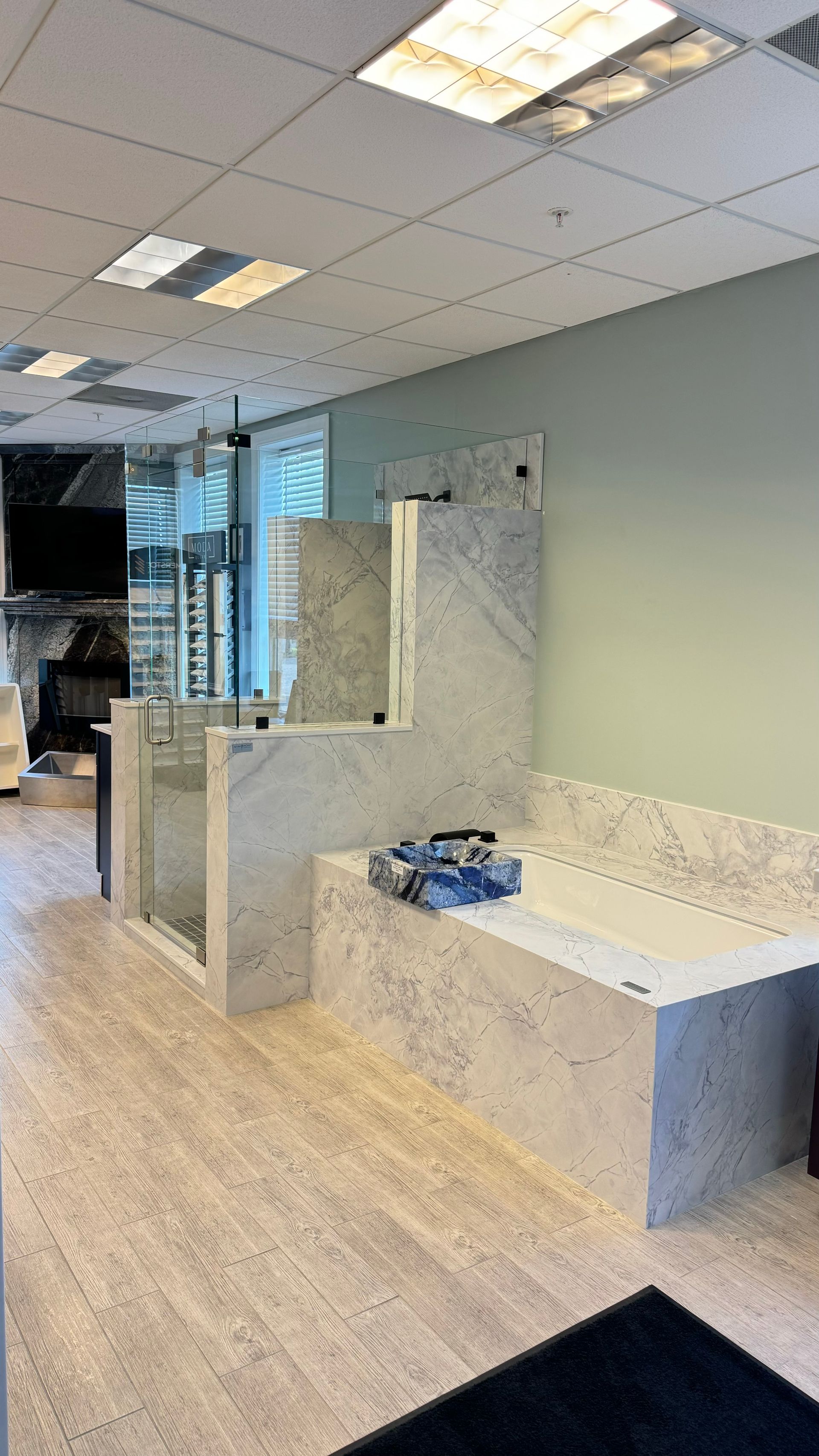 Bathroom with light-colored granite tub and shower, glass enclosures, blue-green walls, and light flooring.