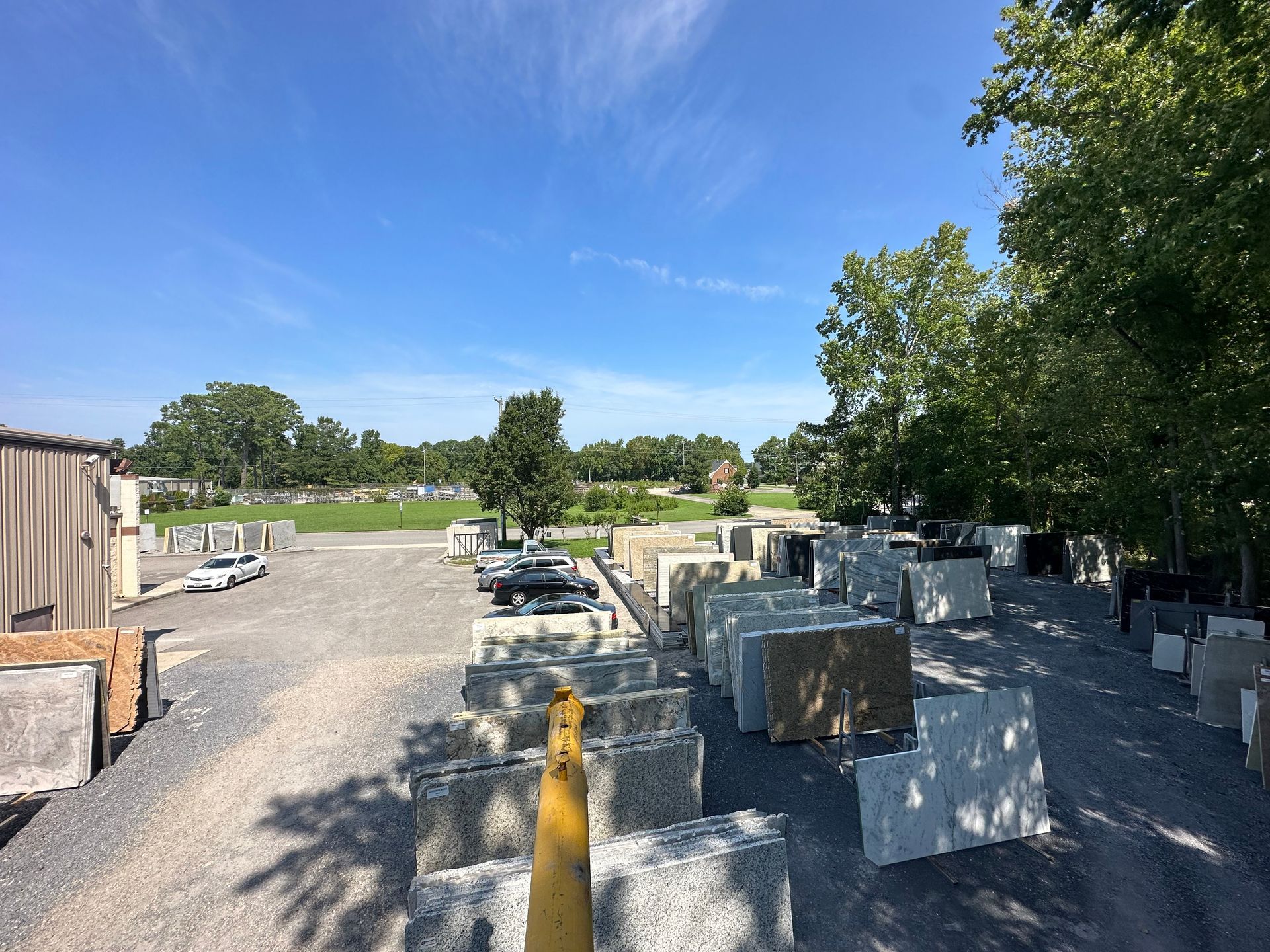 Outdoor stone yard with stacked slabs on gravel, blue sky, and trees.