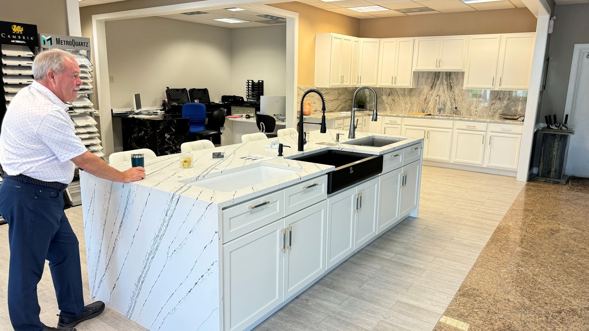 Man examines a white countertop island in a kitchen showroom. Cabinets and sink are white and black.