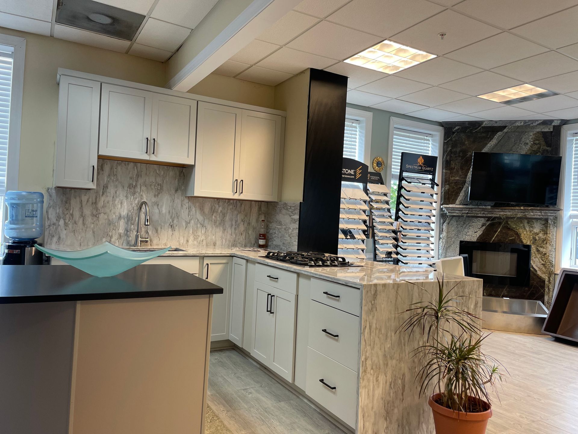 Kitchen showroom with white cabinets, gray countertops, and a stone fireplace.