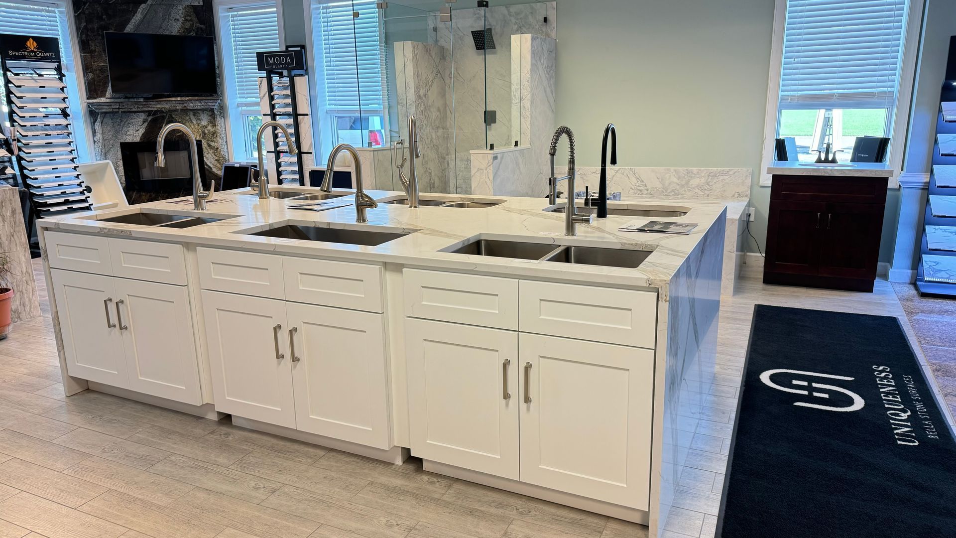 Kitchen sink displays with faucets on white cabinets, showroom setting.