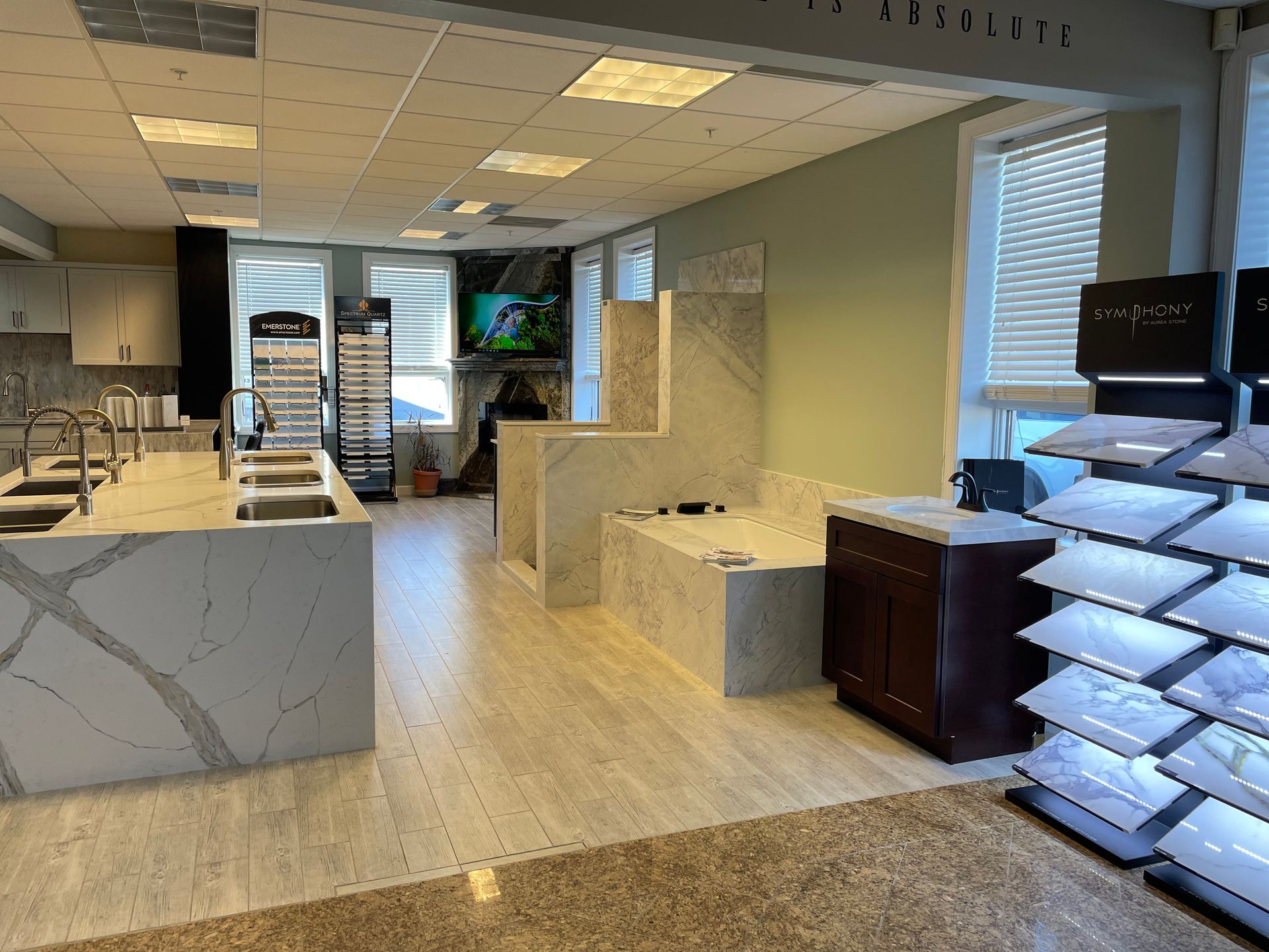 Showroom interior with countertops, sinks, sample displays, and a fireplace. Light wood flooring and neutral walls.