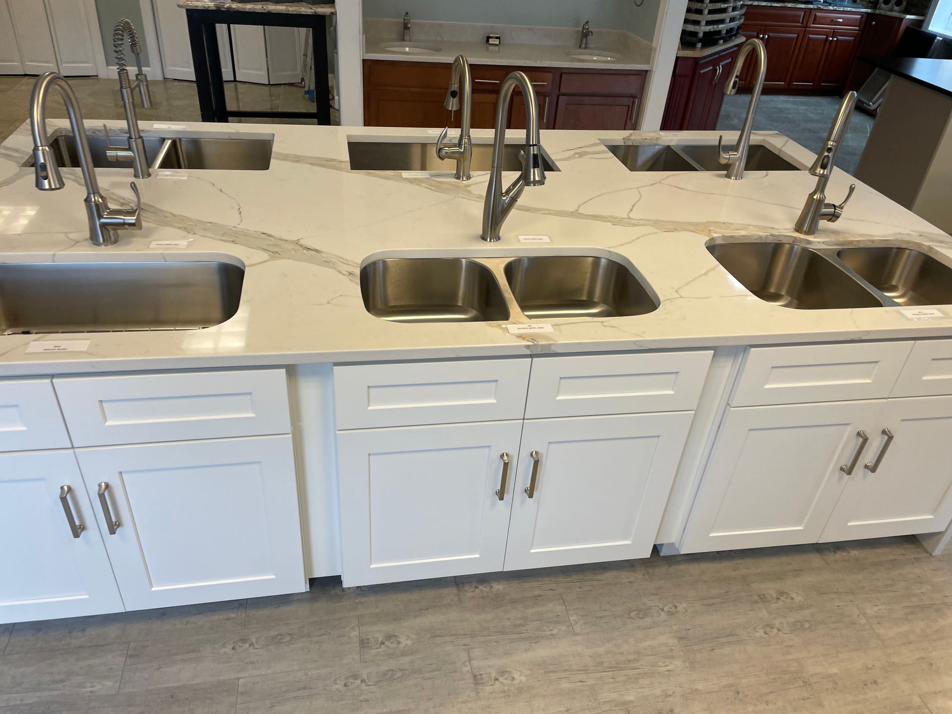 White kitchen island with three sinks and faucets displayed in a showroom.