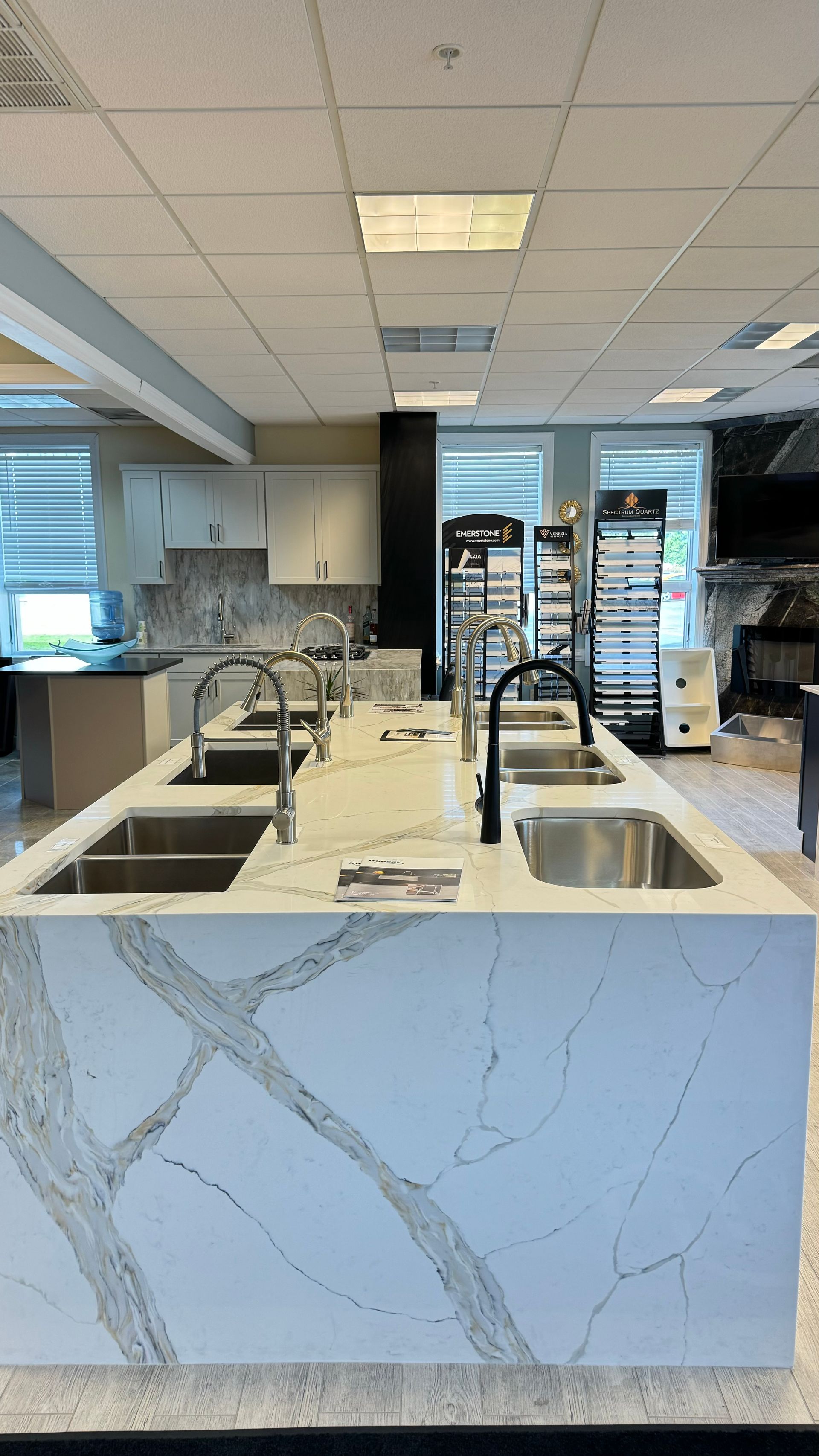 Kitchen island with sinks, faucets, and white countertop with gray veining. Showroom setting.