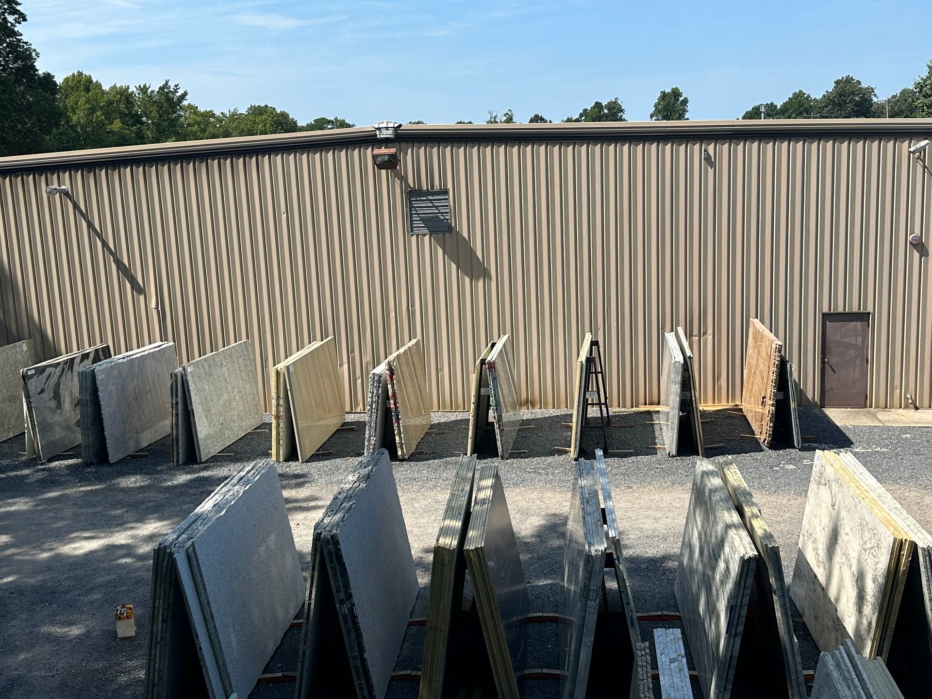 Slabs of stone displayed outside a corrugated metal building on a sunny day.