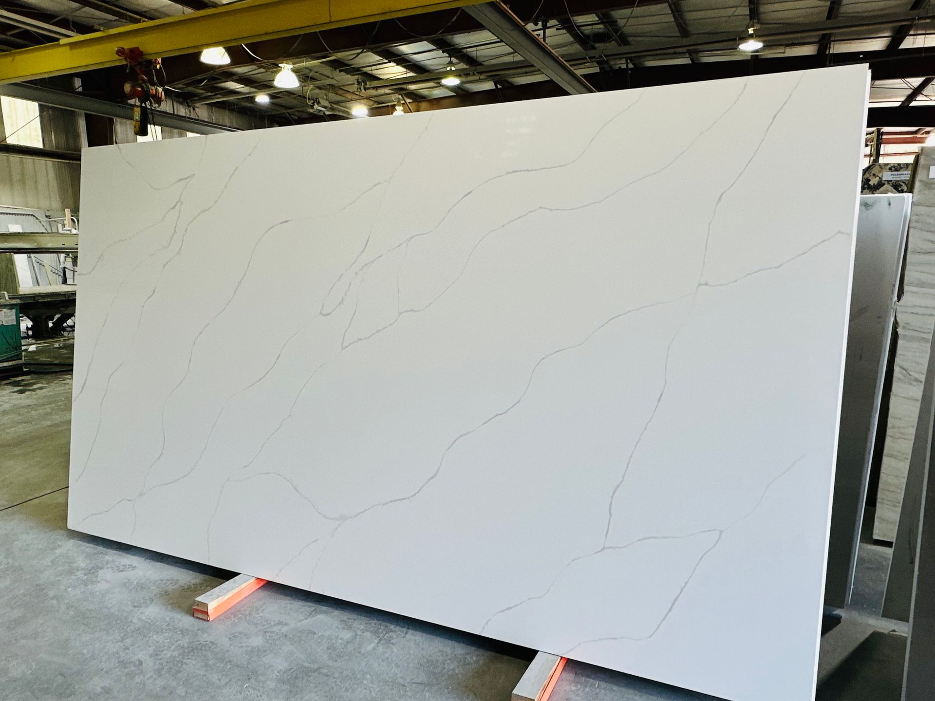 Large white quartz slab with light veining, propped on orange supports in a warehouse setting.
