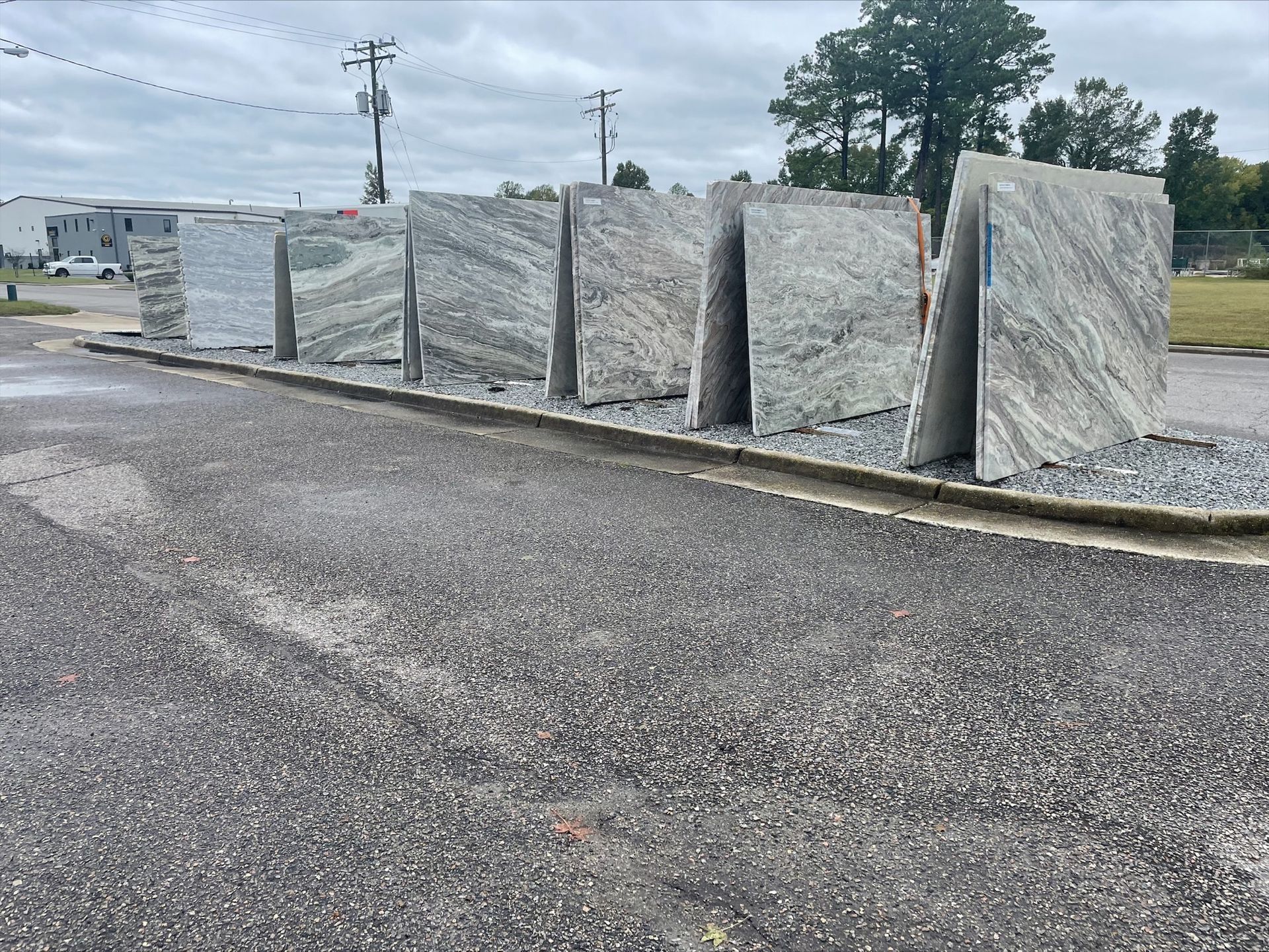 Granite slabs leaning upright on gravel, outdoors.  Various gray and white veined patterns.