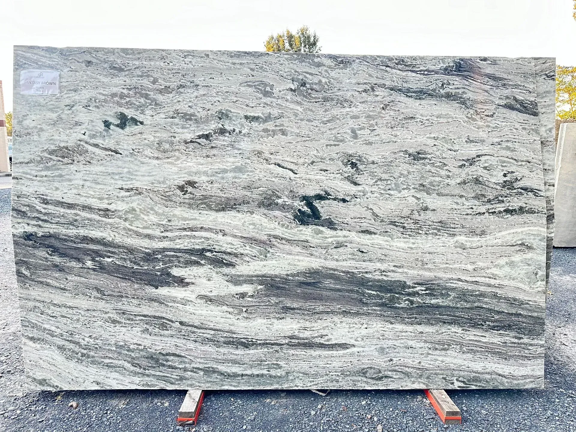 Granite slab with swirling white, gray, and black patterns, displayed on a wooden stand outside.