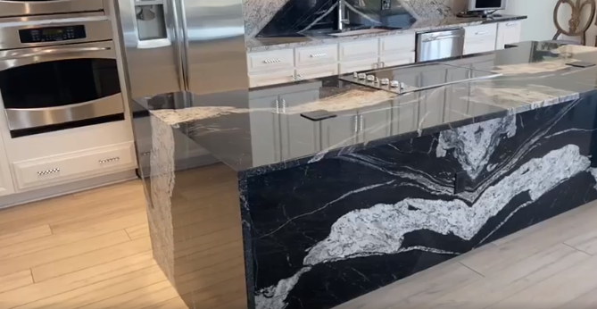 Kitchen island with black and white granite countertop, white cabinets, and stainless steel oven and refrigerator.