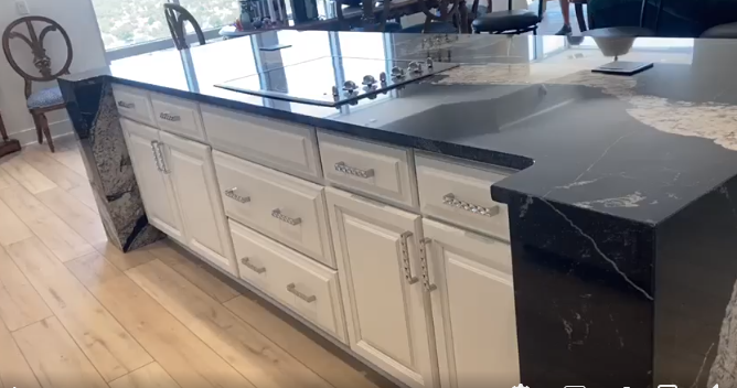 Kitchen island with white cabinets, dark countertops, and built-in stovetop.