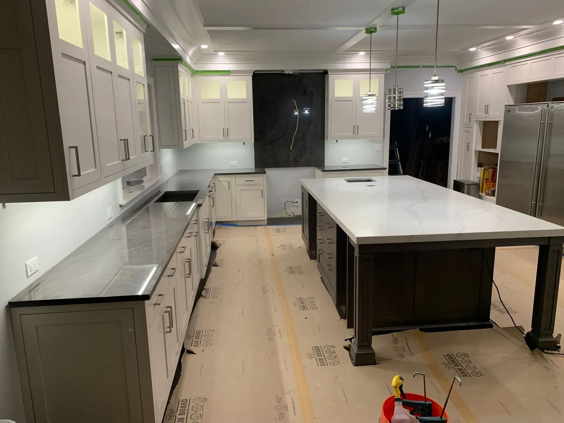 Kitchen under construction with light-colored cabinets, dark countertops, and an island.