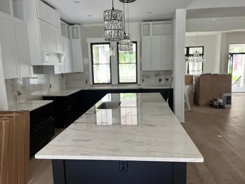 Kitchen with white and dark blue cabinets, marble countertops, pendant lights, and large island.