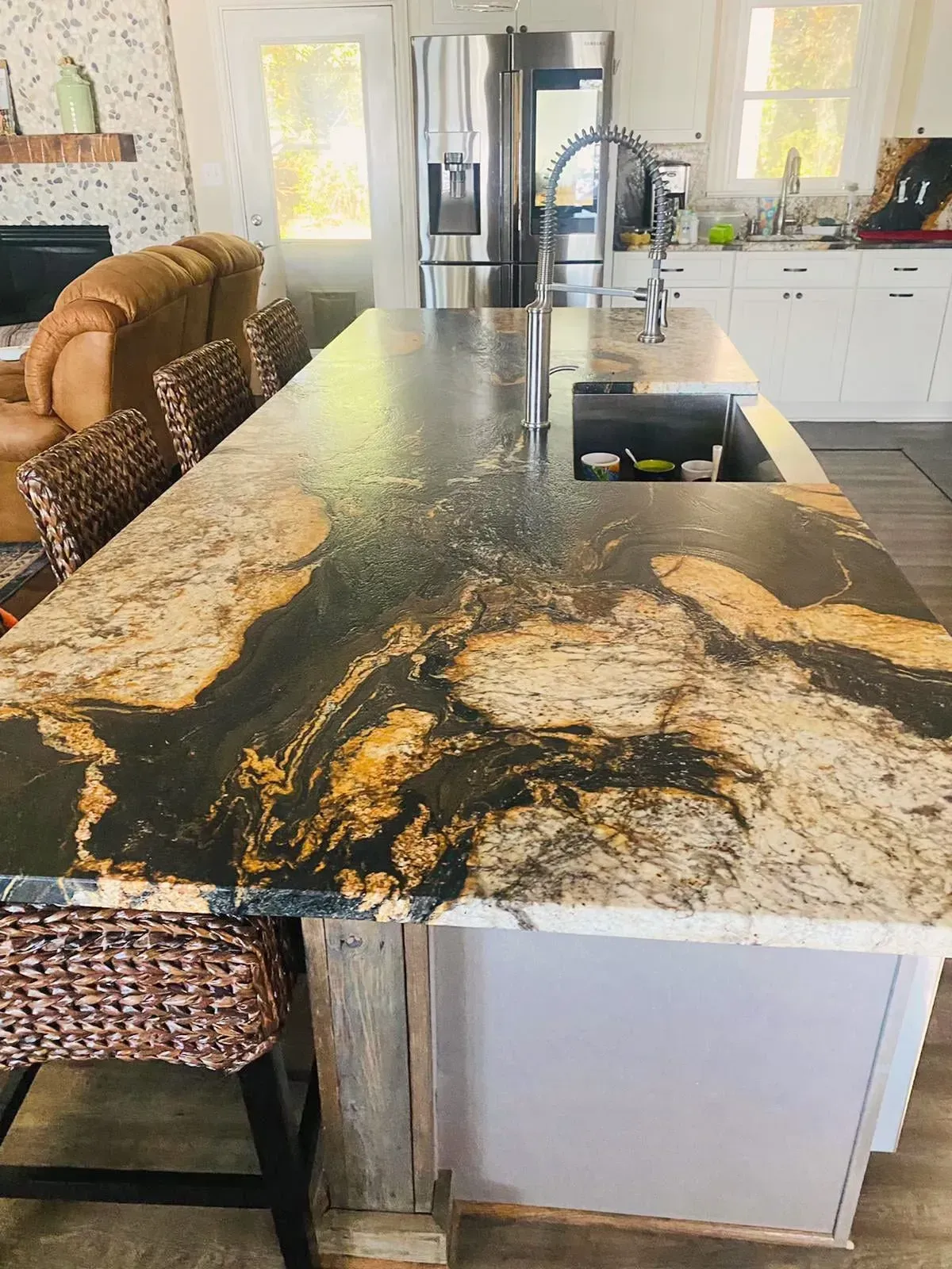 Kitchen island with black and gold granite countertop, stainless steel sink, and bar stools.