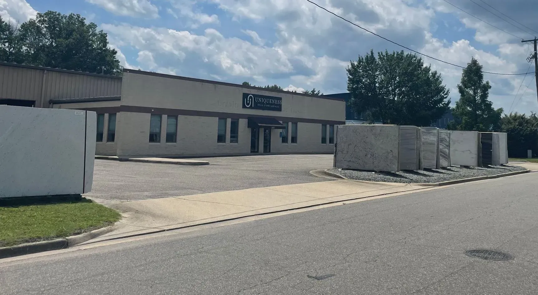 A business building with a sign and stacks of building materials in front, seen from the street.