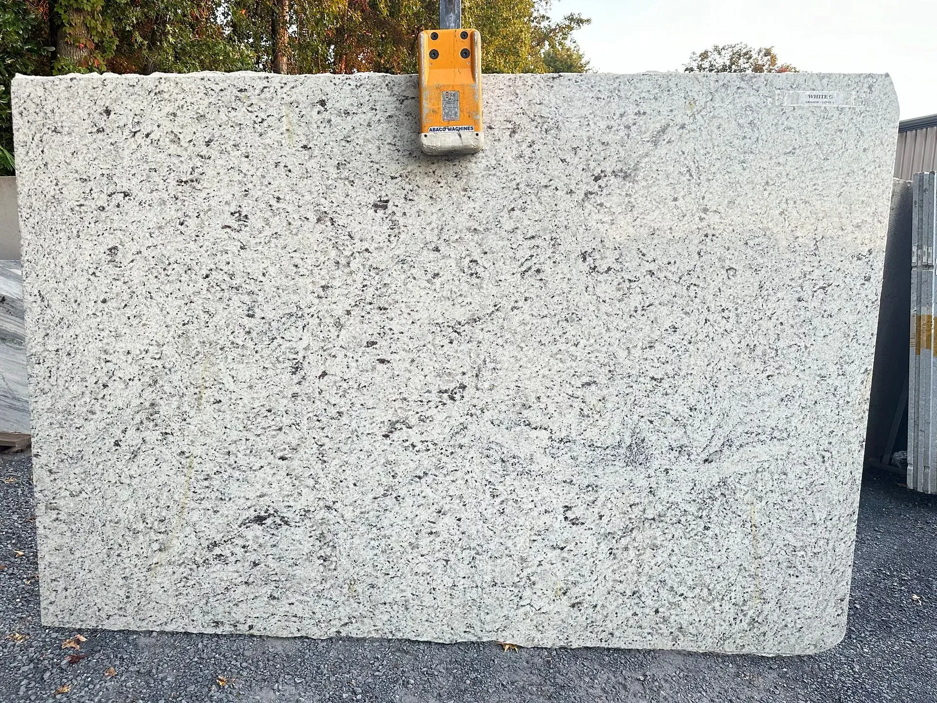 Large white granite slab with dark speckles, being lifted by a yellow crane.