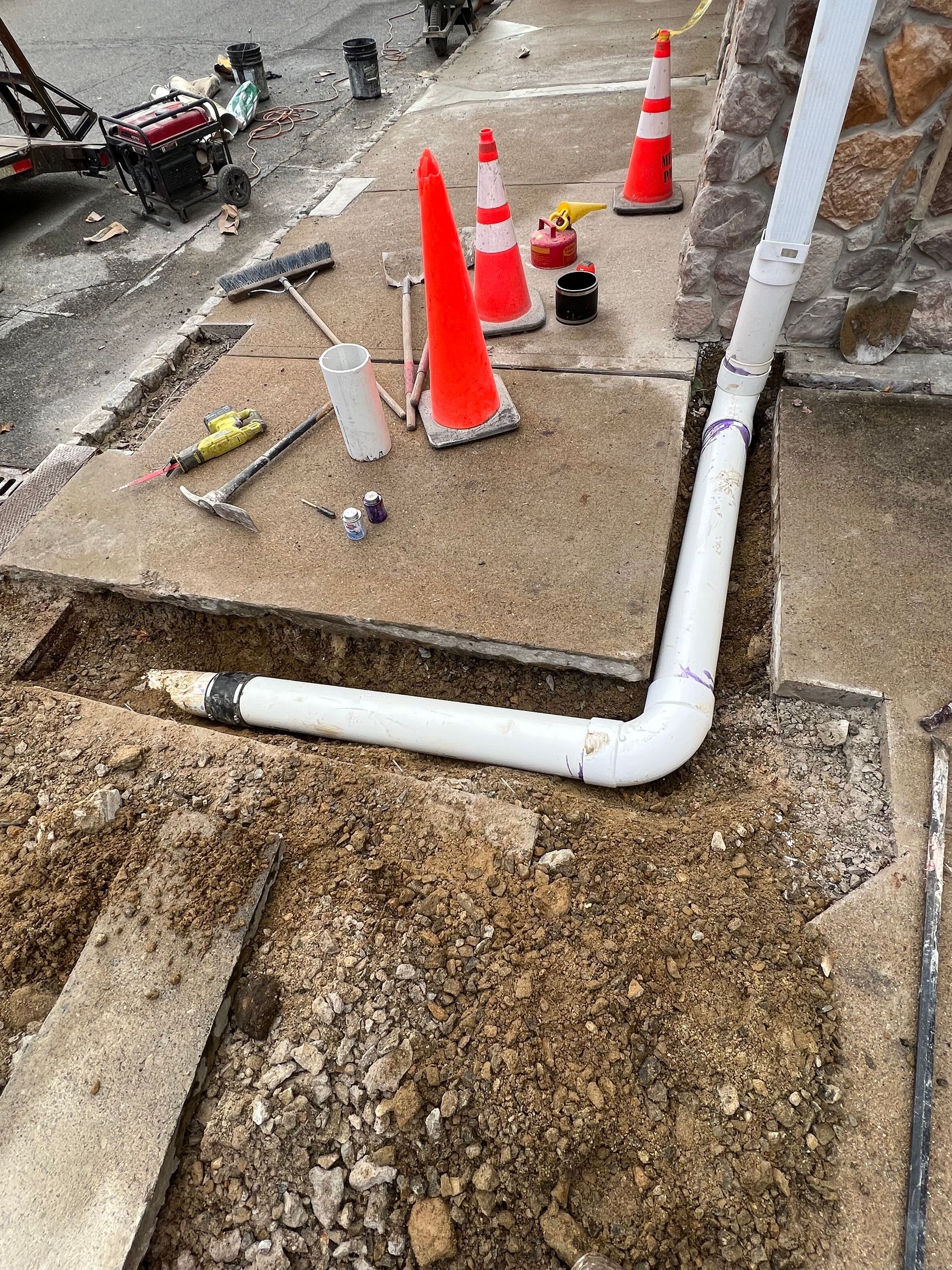 A drain pipe is being installed on the sidewalk next to a building.