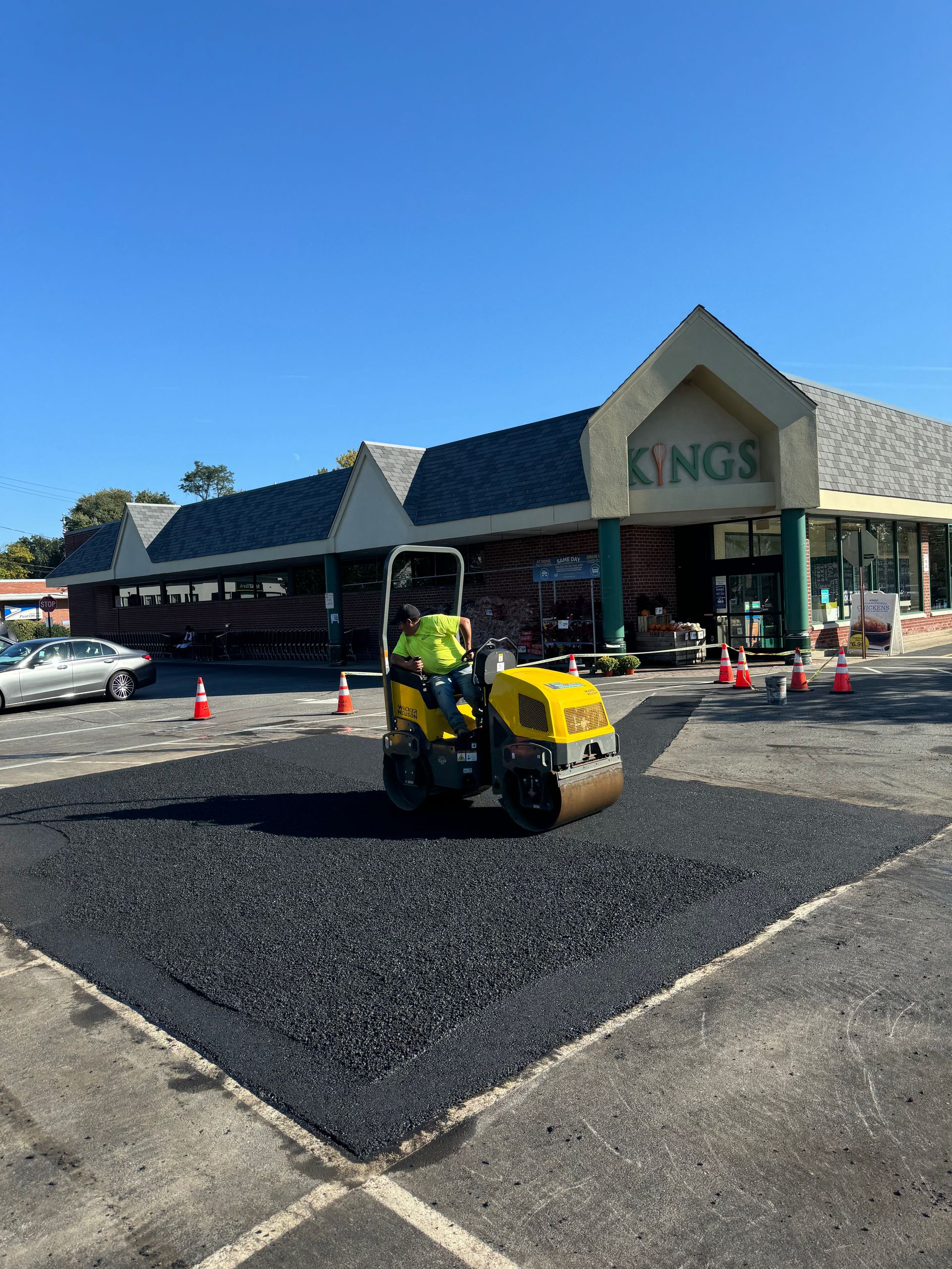 A yellow roller is rolling asphalt in front of a store.